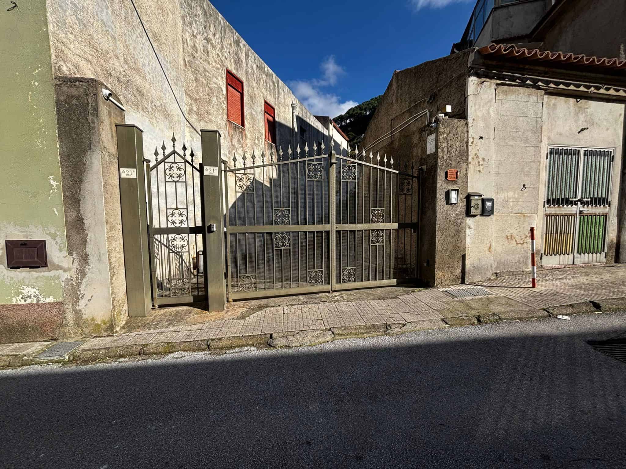 Cancello in metallo con design elegante, accesso a proprietà residenziale in zona urbana, sicurezza e privacy, con imponente parete in pietra e elementi di recinzione moderni.