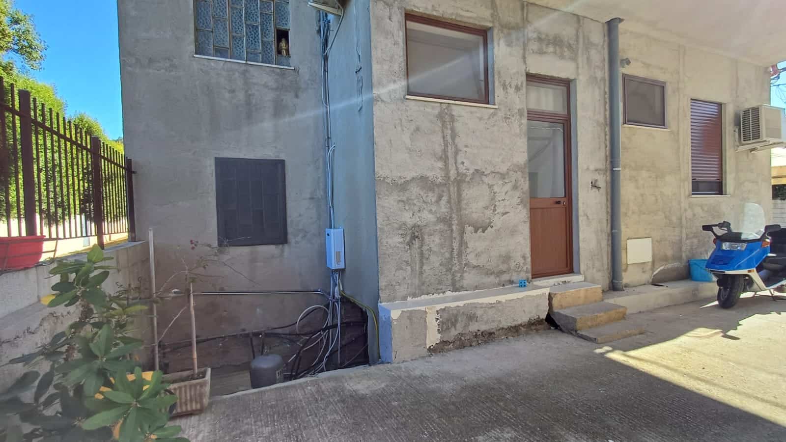 Immagine di una parete esterna di una casa in costruzione o ristrutturazione, con cavi elettrici e finestra, ambientazione urbana, dettagli di lavori edilizi, con scooter parcheggiato sul lato.