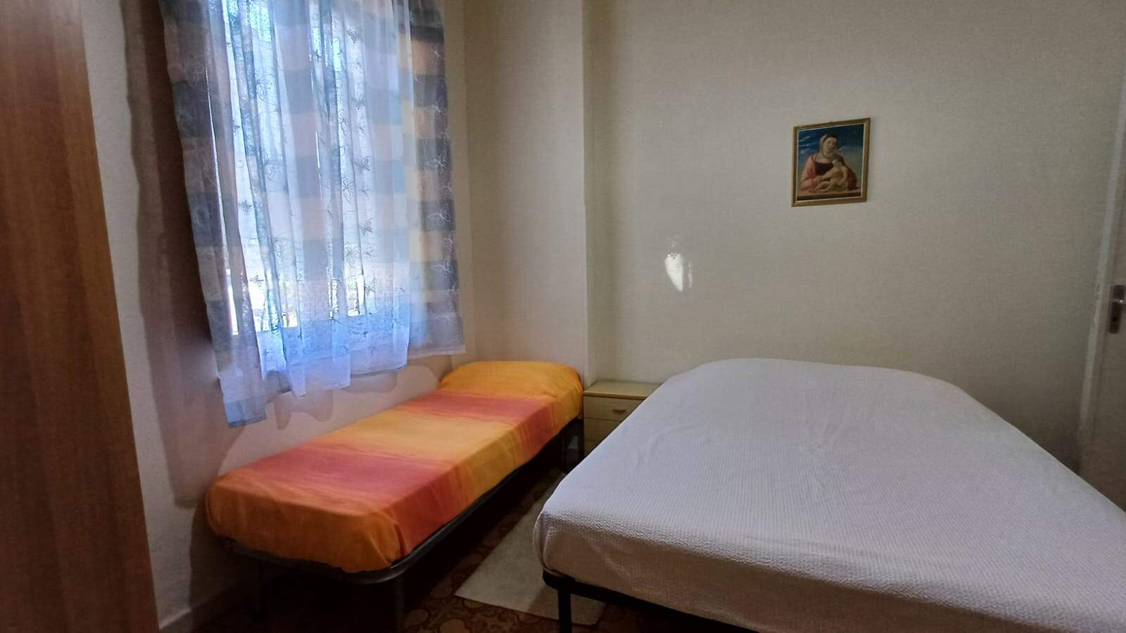 Sistemazione semplice con due letti singoli e una finestra con tende in una camera da letto. Ideale per soggiorni brevi o ospiti, ambientazione accogliente e funzionale, perfetta per chi cerca comfort in affitto a breve termine.