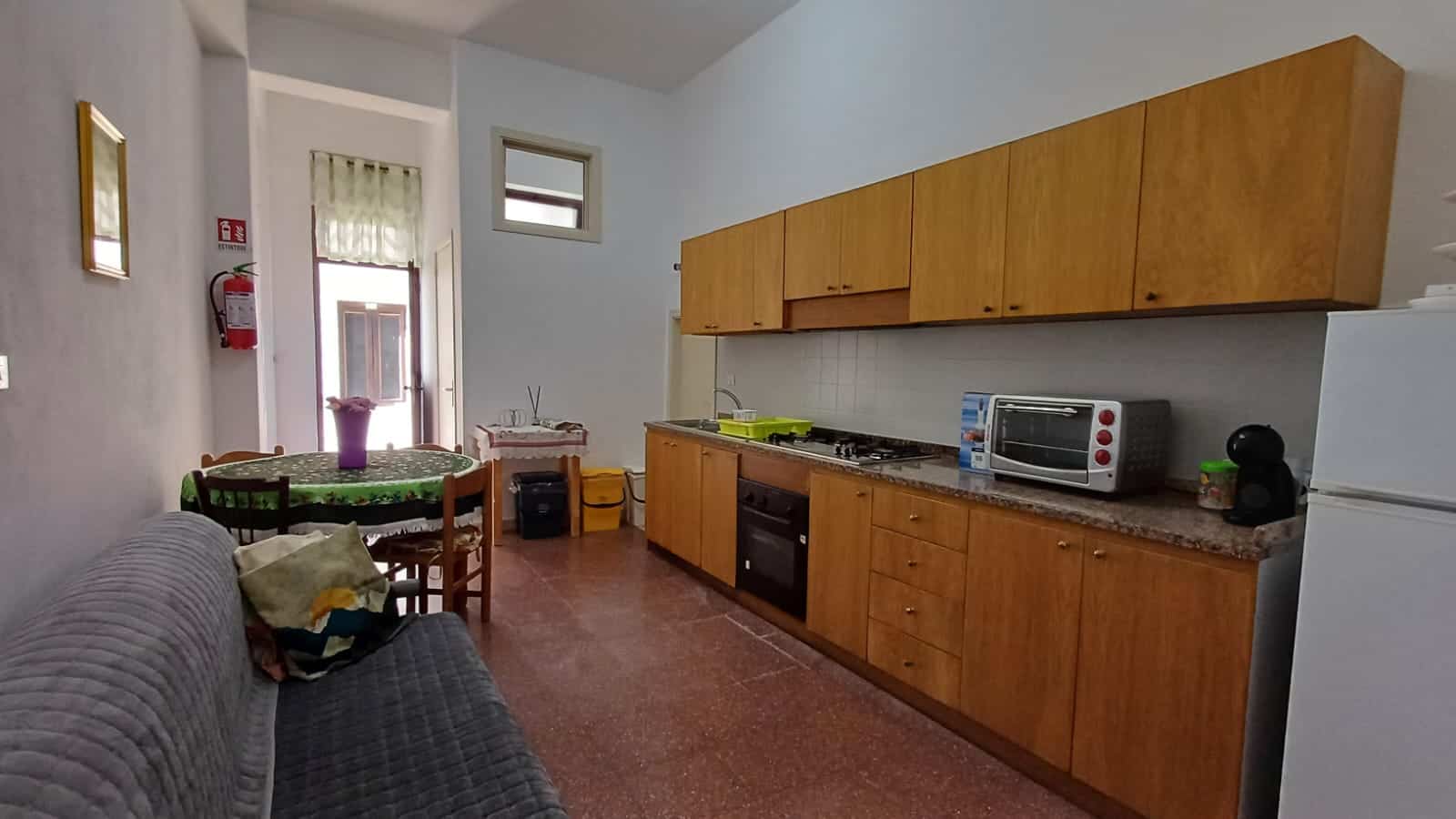 Spazio cucina abitabile con mobili in legno, piano cottura e forno, tavolo da pranzo con sedie, ideale per affitti case vacanza NextCasa in Italia.