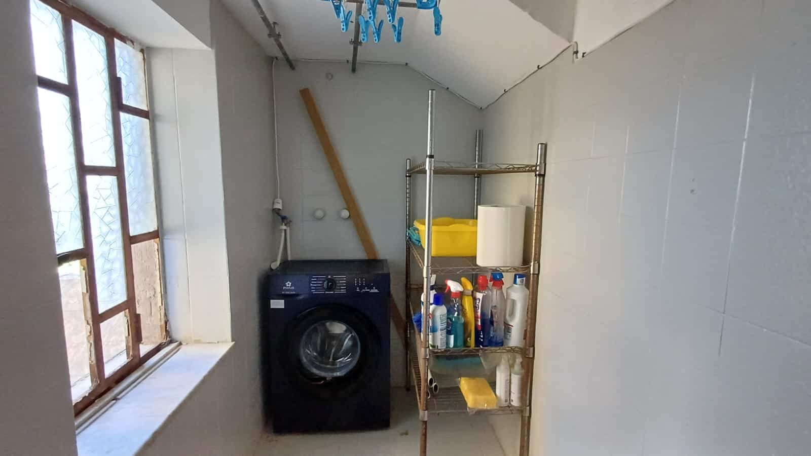 Lavanderia con lavatrice, scaffale con detersivi e ricambi, ampia finestra per ventilazione naturale, spazio pratico e funzionale per la gestione della casa, ideale per la zona lavanderia e stiro.