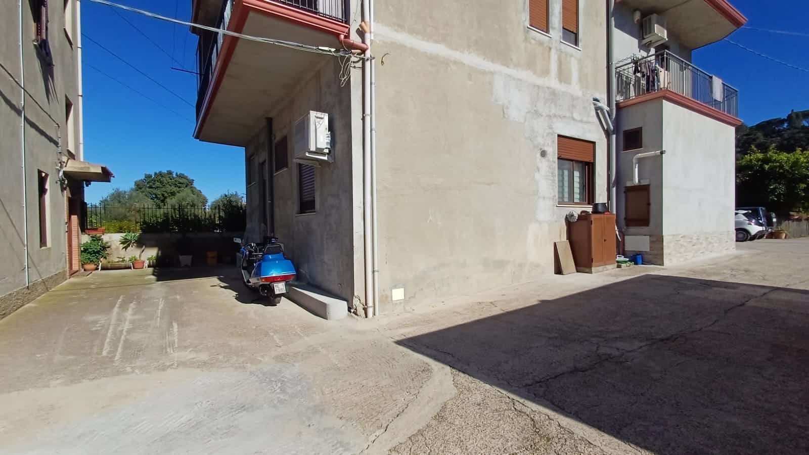 Auto di cortesia parcheggiata all'esterno di un edificio residenziale con balconi, zona di parcheggio privata e ambiente urbano tranquillo vicino al verde.