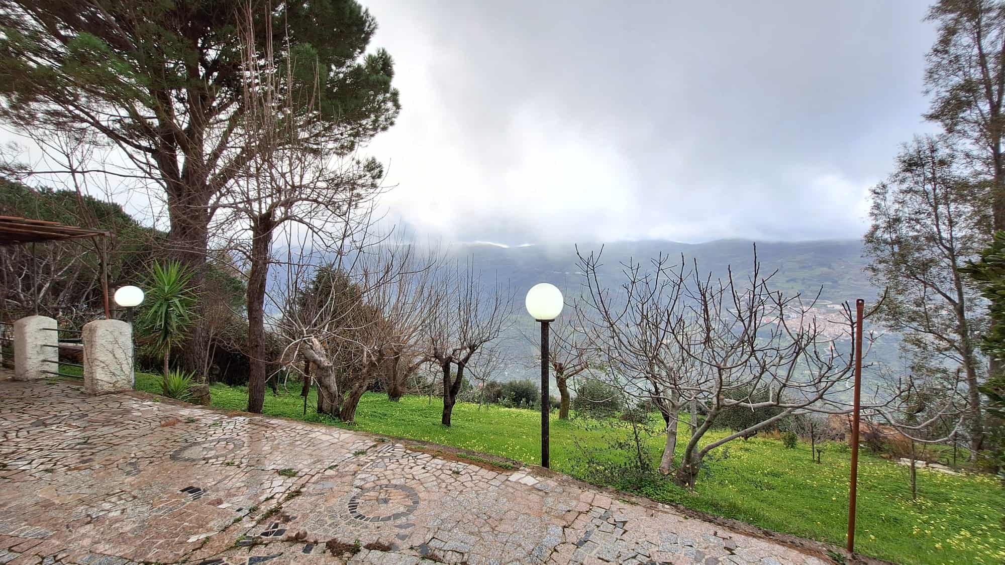 Verde giardino con alberi e pietre, luci da esterno in stile lampione, splendida vista montagna nebbiosa, ideale per case in vendita o affitto in contesti naturali; panorama rilassante e naturale.