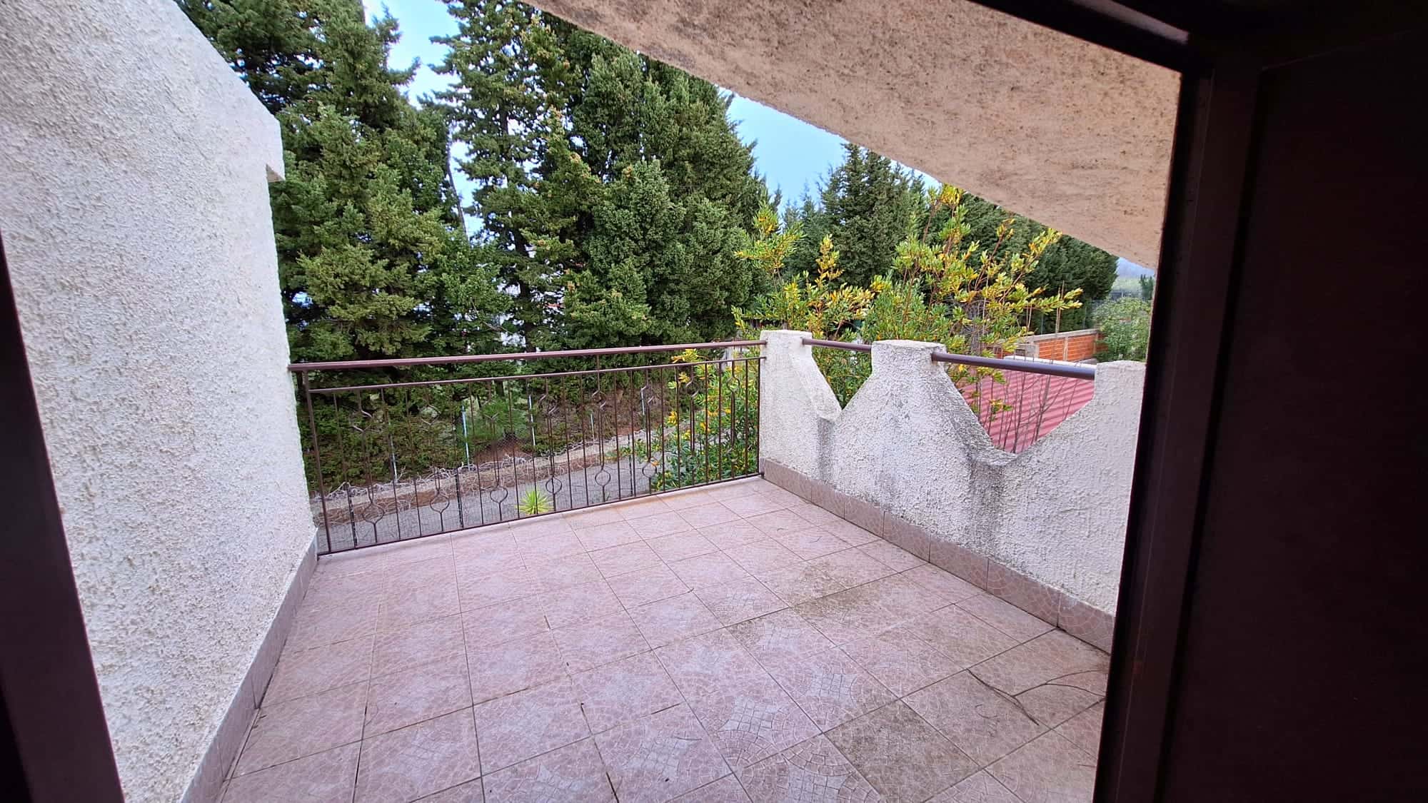 Balcone esterno con vista su alberi e natura, ideale per relax e momenti di tranquillità in casa. Design semplice con ringhiera in metallo e pavimentazione in piastrelle.