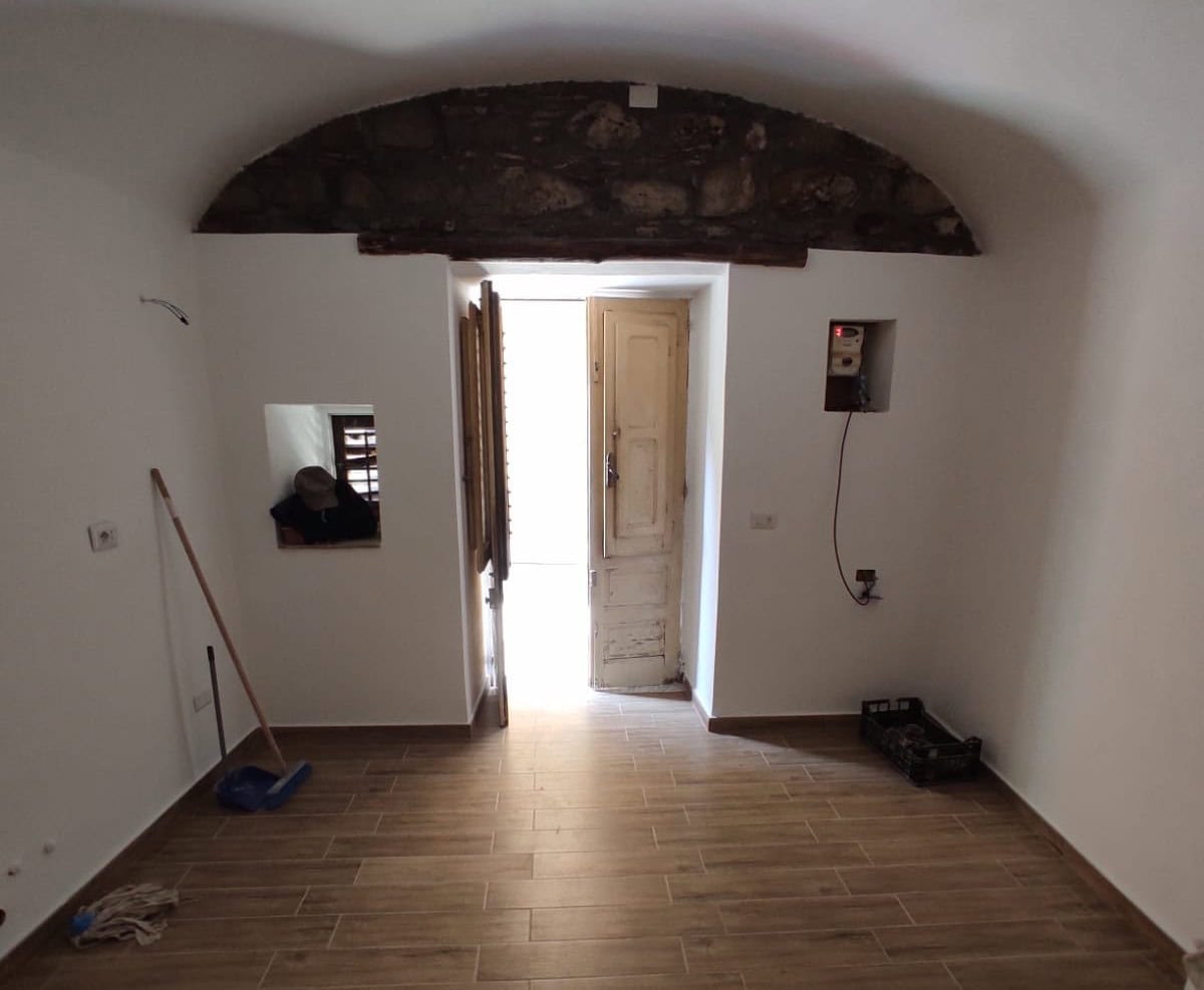 _scanalatura in muro di casa ristrutturata con arco in pietra, porta in legno e parquet, ambiente luminoso e accogliente, ideale per interni di proprietà NextCasa_.