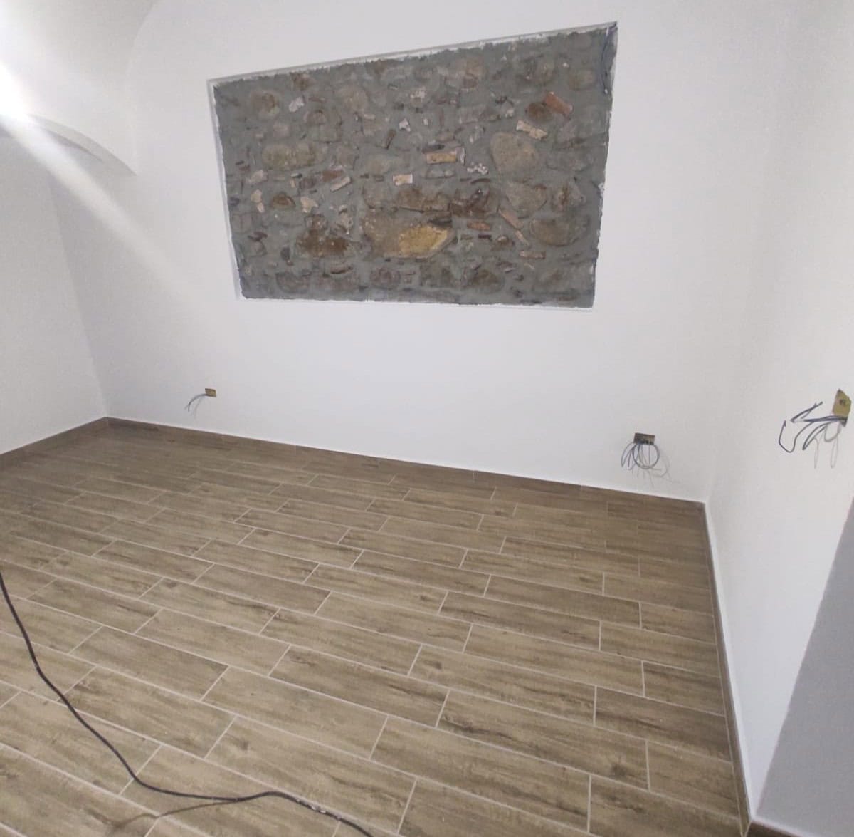 1. Finestra sul soffitto con mattoni a vista in un interno di casa in fase di ristrutturazione, pavimento in gres effetto legno e pareti bianche.