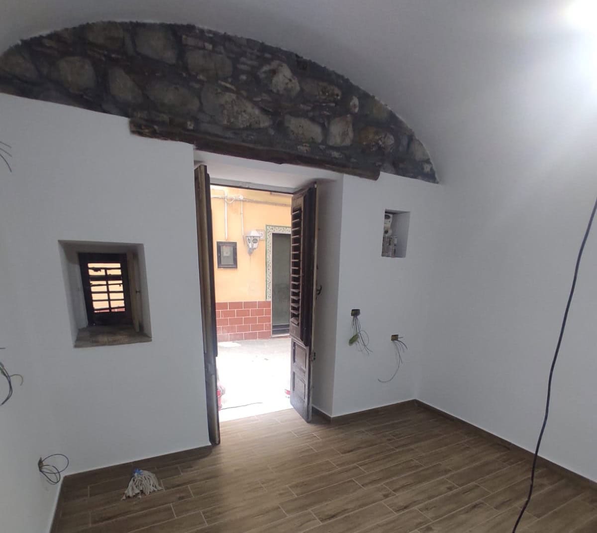 1. Trave in pietra a vista nel soffitto di una stanza in fase di ristrutturazione, con pareti bianche e pavimento in gres effetto legno.