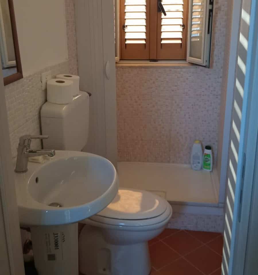 Bathroom con servizi igienici e doccia, ambiente luminoso con finestra in legno e arredo funzionale, ideale per soluzioni abitative moderne e confortevoli.