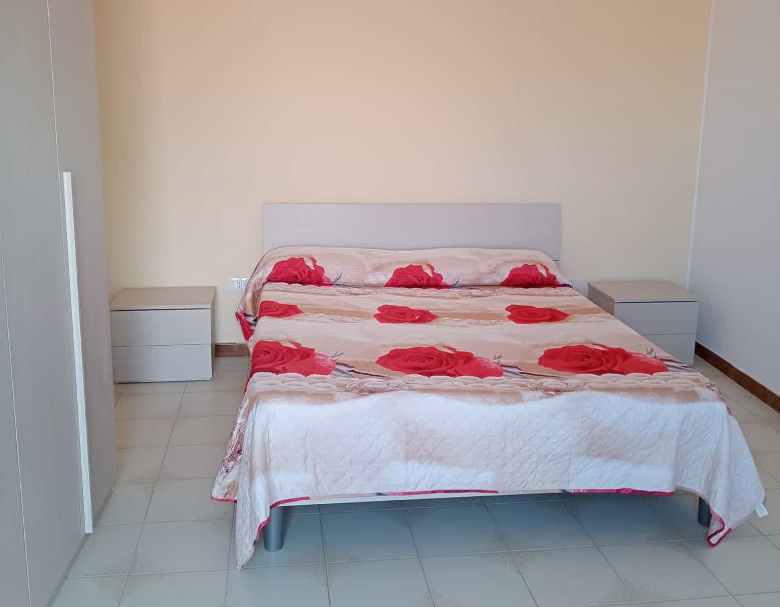 Letto matrimoniale con coperta a rose rosse, camera da letto moderna, arredamento minimalista, mobili in stile contemporaneo, alloggio in affitto o vendita, interior design elegante, NextCasa, appartamento confortevole.