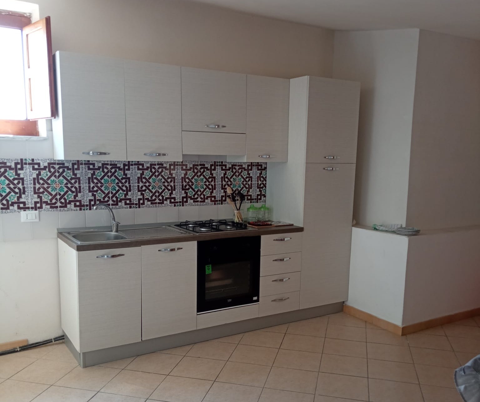 Cucina moderna con pensili bianchi, piano in legno e piastrelle decorative sullo sfondo, dotata di forno, piano cottura e lavabo, in un ambiente luminoso e accogliente.