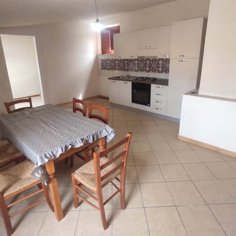 1. Cucina abitabile con mobili bianchi, piano cottura e arredamento semplice, spazio di soggiorno luminoso e parete con rivestimento decorativo in stile tradizionale italiano.