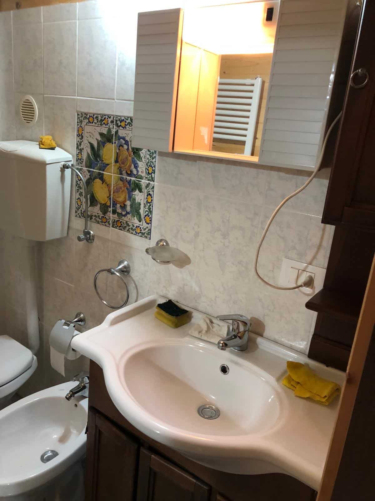 Lavandino bagno con specchio e mobili in stile rustico, dettagli di colore e funzionalità in ambiente di proprietà NextCasa.