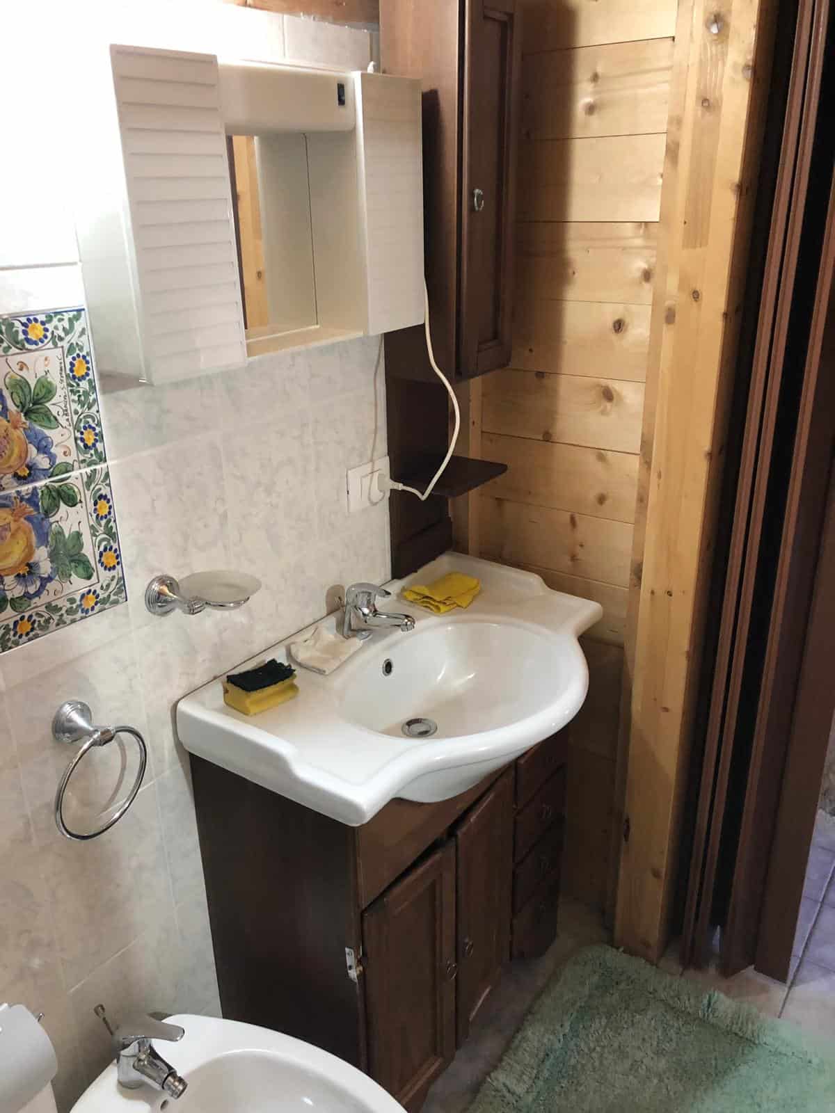 Specchio e mobile bagno in stile rustico con lavabo in ceramica, dettagli in legno, ambiente accogliente e funzionale, perfetto per bagni in case di montagna o chalet, con accessori coordinati e panno in tessuto naturale.