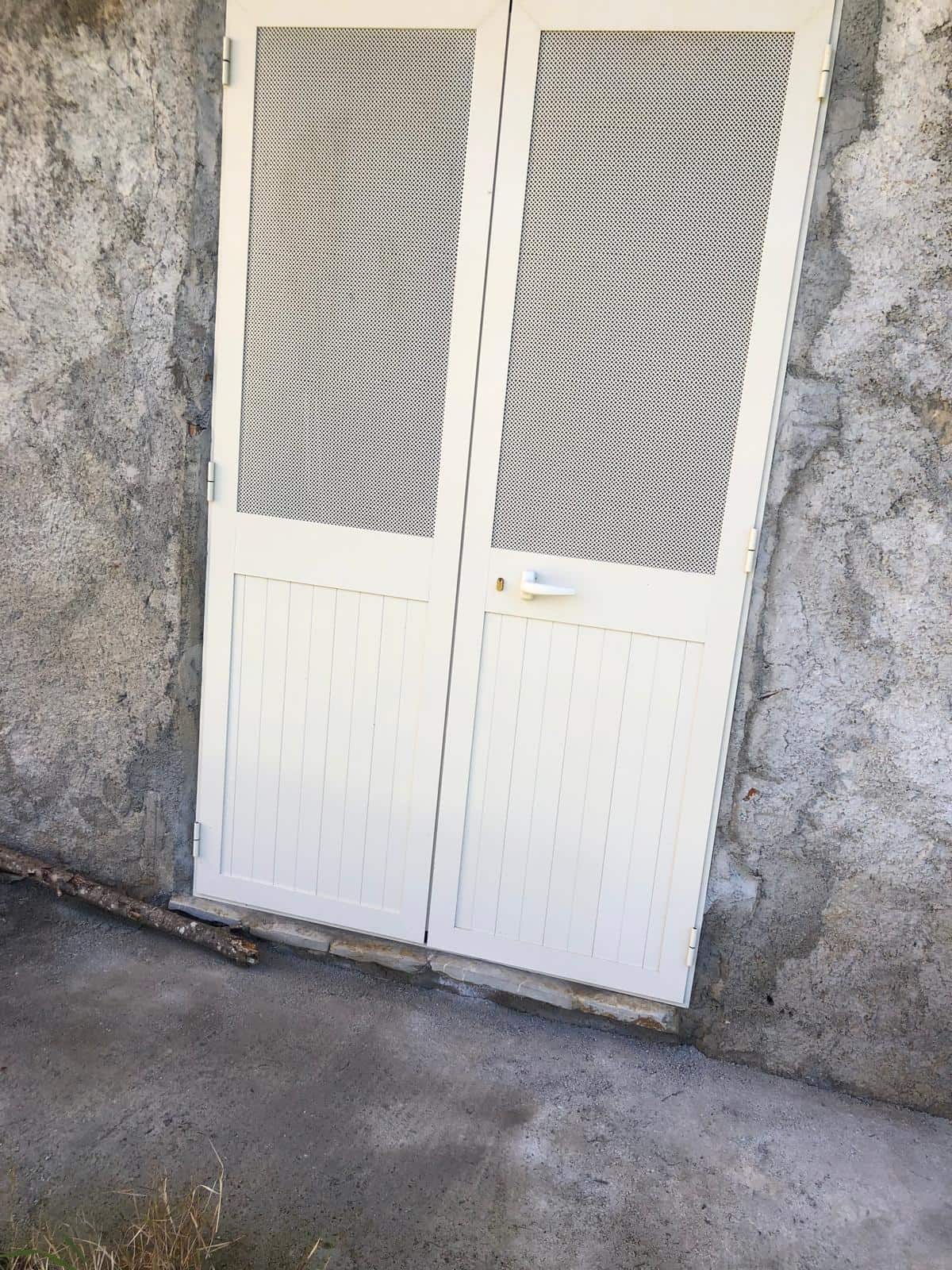 Cancello bianco in metallo con grigliato, installato su parete in cemento, ideale per sicurezza e privacy in residenze e immobili commerciali.