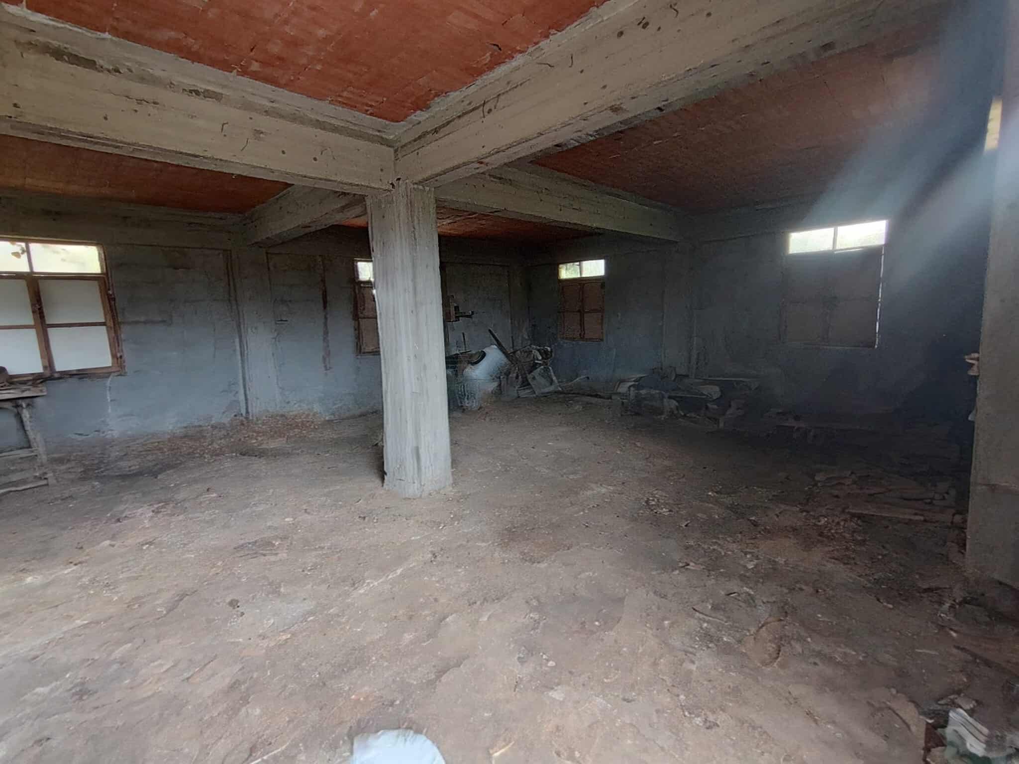 Vecchio capannone industriale in costruzione, spazio ampio con muri in cemento e soffitto a vista in legno, illuminato dalla luce naturale tramite finestre. Ideale per ristrutturazione e trasformazione in immobile residenziale o commerciale.