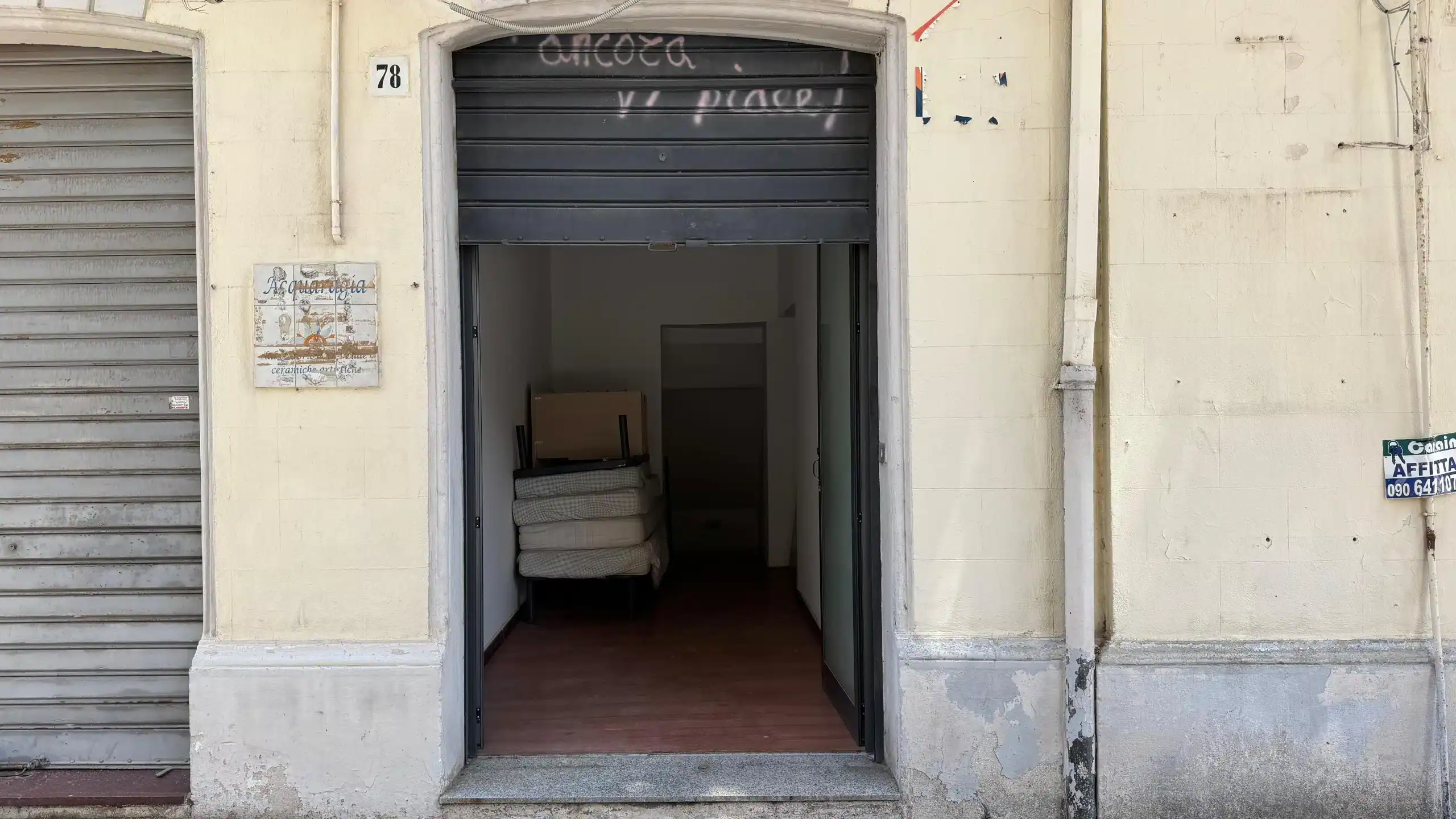 1. Entrata di un negozio di arredamento NextCasa con porta socchiusa, pareti beige e ambiente interno visibile.