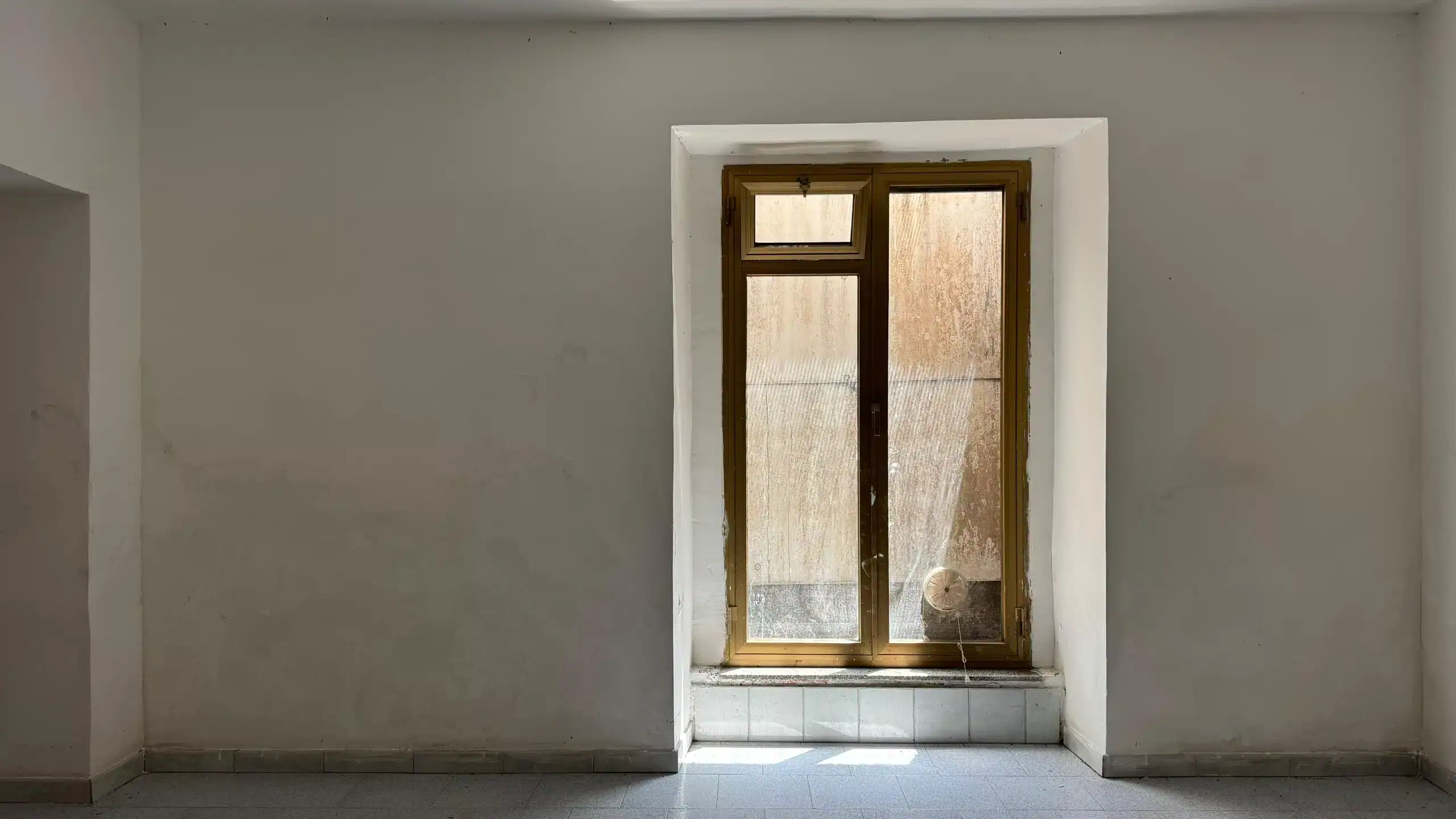 1. Finestra in una stanza vuota con pareti bianche e pavimento in piastrelle, luce naturale che entra attraverso il vetro.