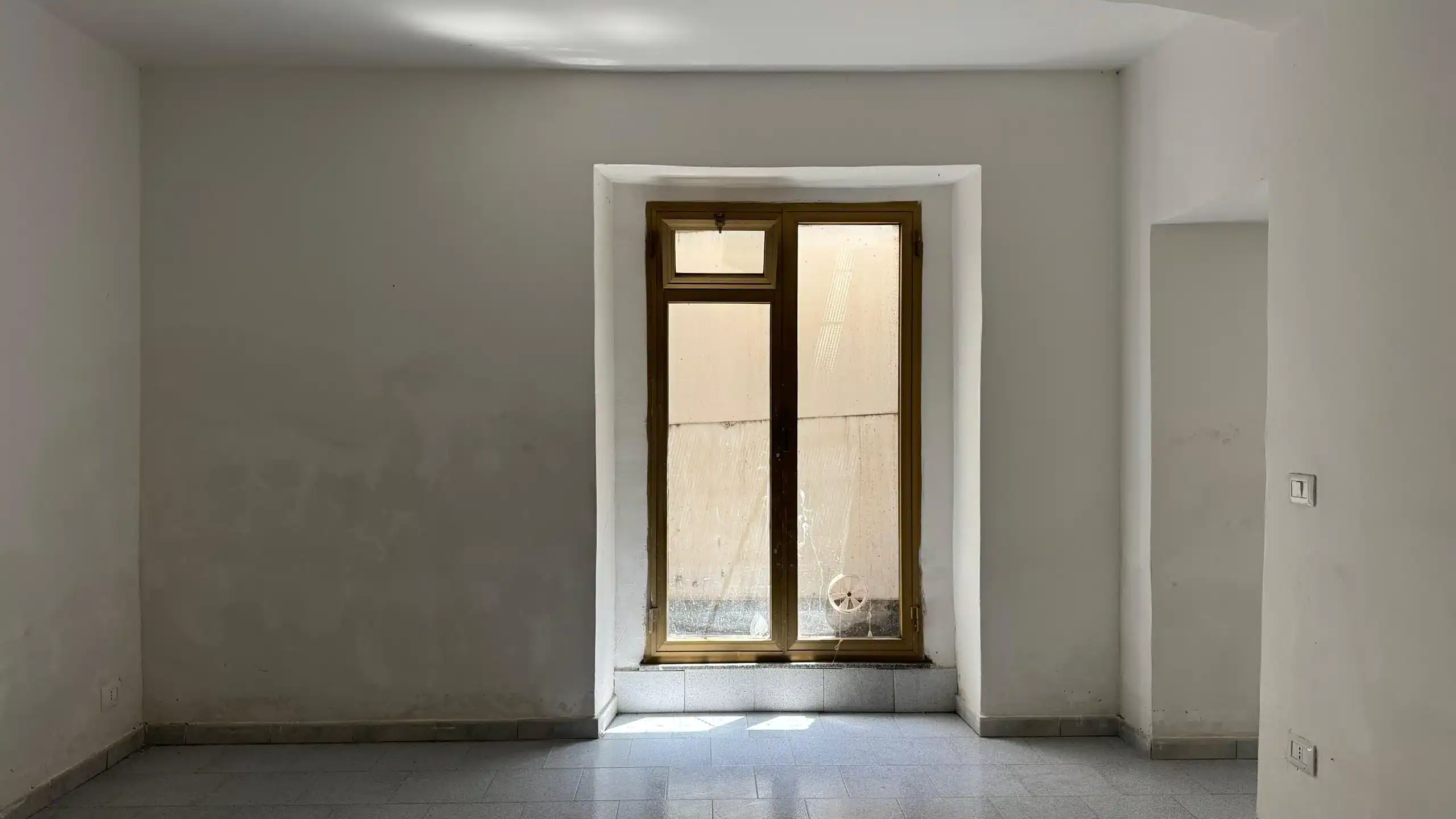 Finestra in una stanza vuota con pareti bianche, luce naturale, pavimento in piastrelle, pronto per ristrutturazione o arredamento, ideale per realizzare la casa dei sogni.