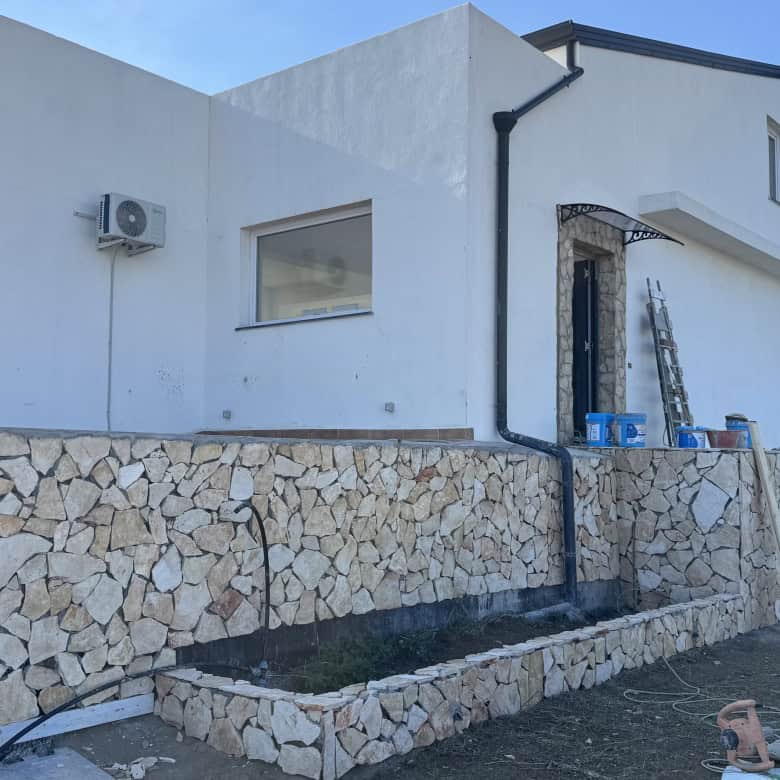 Parete esterna moderna di casa in costruzione con dettagli ristrutturazione, muri in pietra e finiture bianche, ideale per progetto immobiliare di alta qualità.