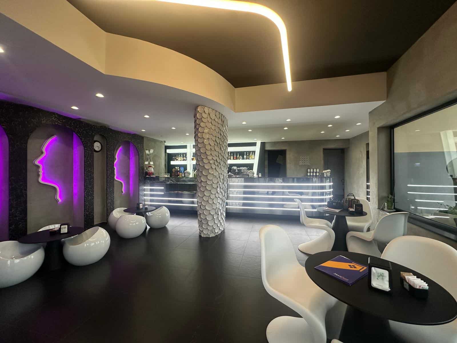 Bar lounge moderno con sedute bianche e illuminazione rosa, atmosfera sofisticata e accogliente, ideale per aperitivi e incontri sociali in un ambiente di tendenza.