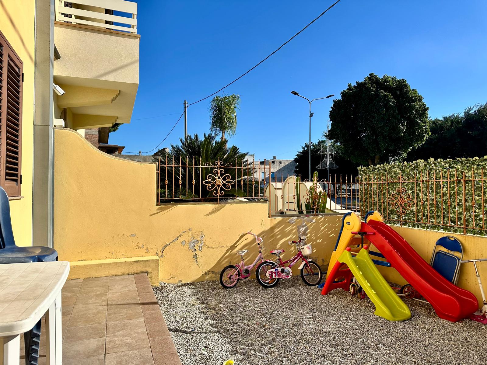 Giardino per bambini con altalena scivolo e biciclette, zona esterna ben curata, ambiente familiare e sicuro, ideale per giochi e tempo libero all'aperto.