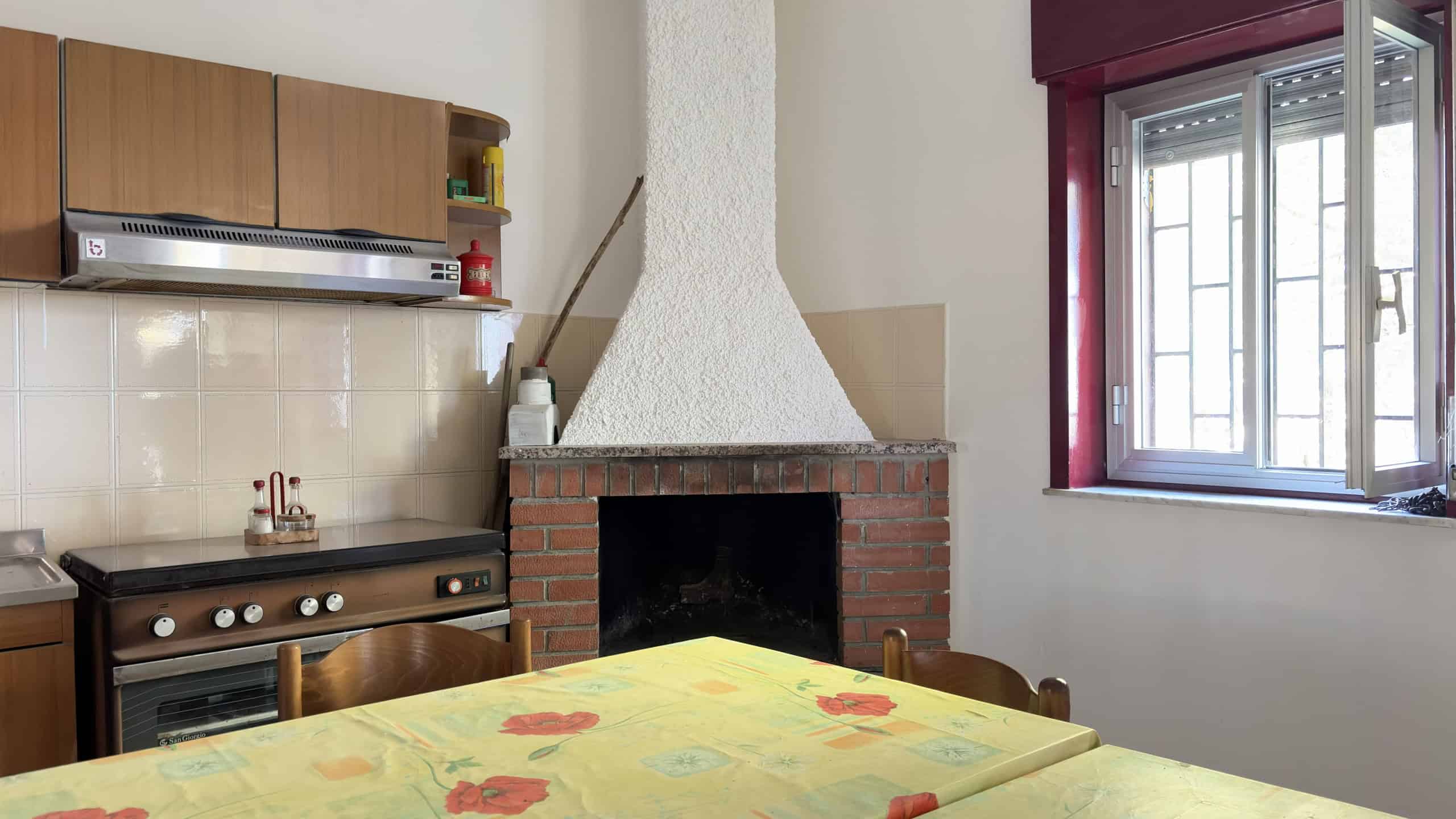 Accogliente cucina rustica con camino in mattoni, stufa a gas e finestra grande, ideale per case vacanza e appartamenti in affitto su NextCasa.