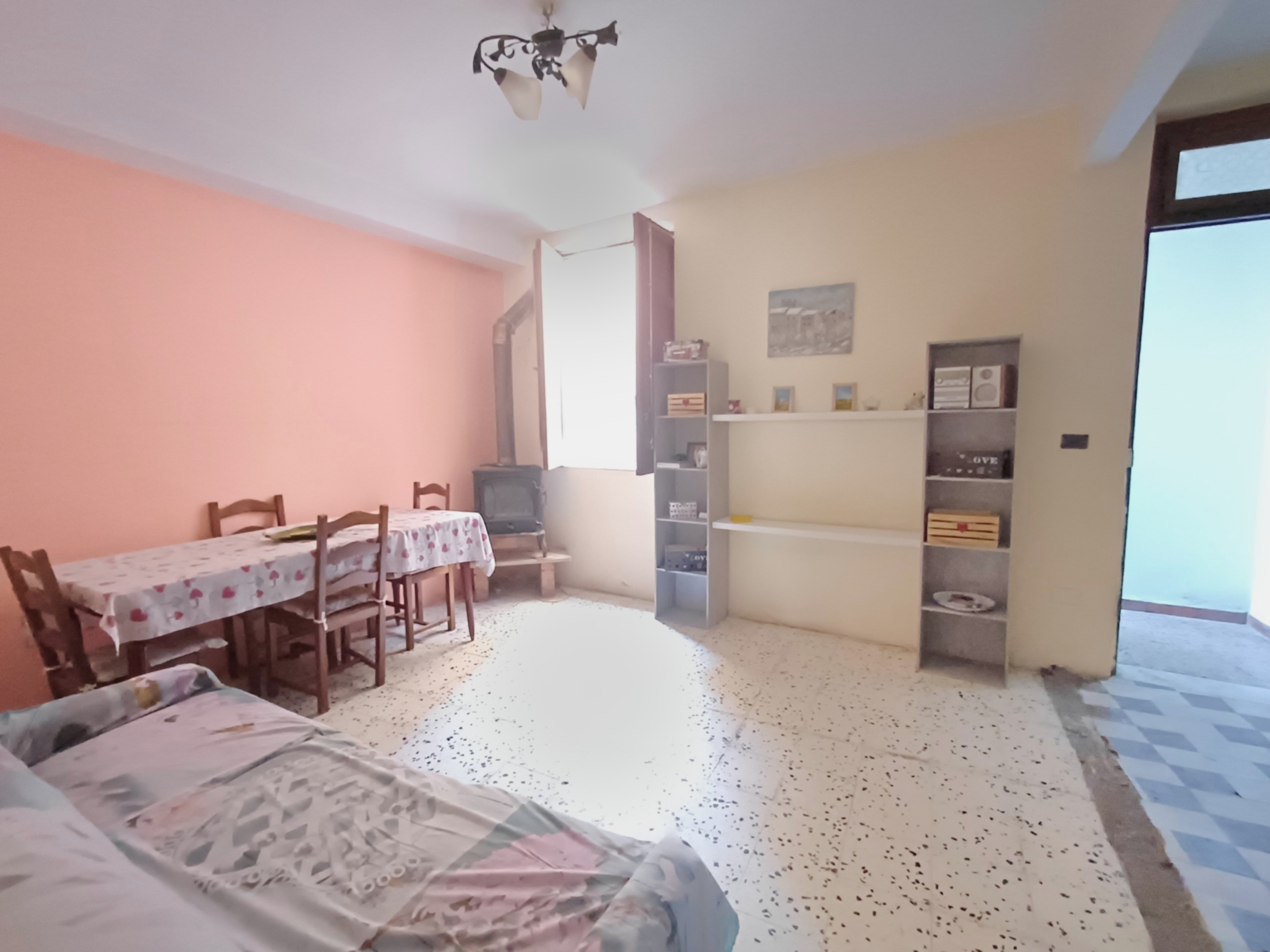 Ampio soggiorno con pareti color pesca, tavolo da pranzo con tovaglia floreale, mobili semplici, soggiorno e zona pranzo luminosa e accogliente, ideale per famiglie e case con stile pratico.
