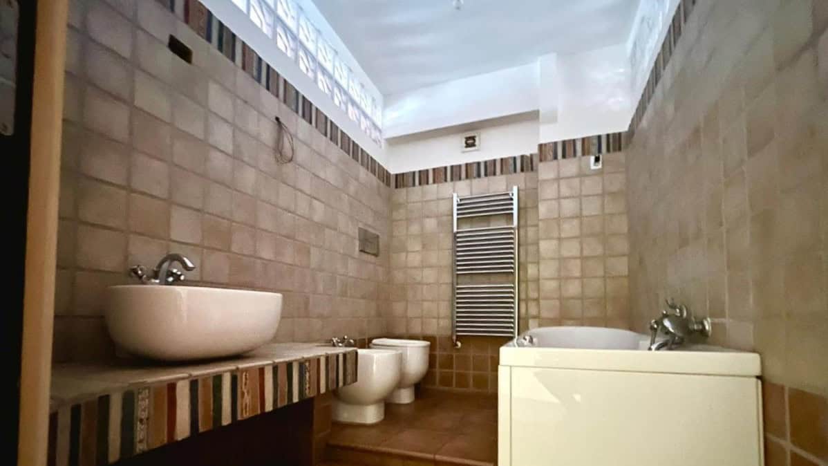 Lavabo, bidet e vasca da bagno in stile rustico, bagno moderno con pareti in cotto e elemento riscaldante in acciaio, ambiente accogliente e funzionale.