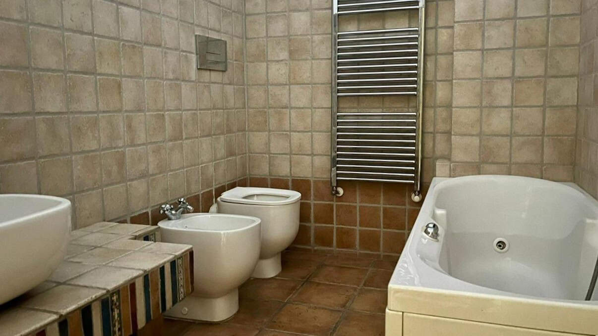 Bagno moderno con vasca idromassaggio, bidet e asciugatrice in acciaio inox, pareti e pavimenti in ceramica beige, stile rustico, spazio ben organizzato, arredamento funzionale e elegante.