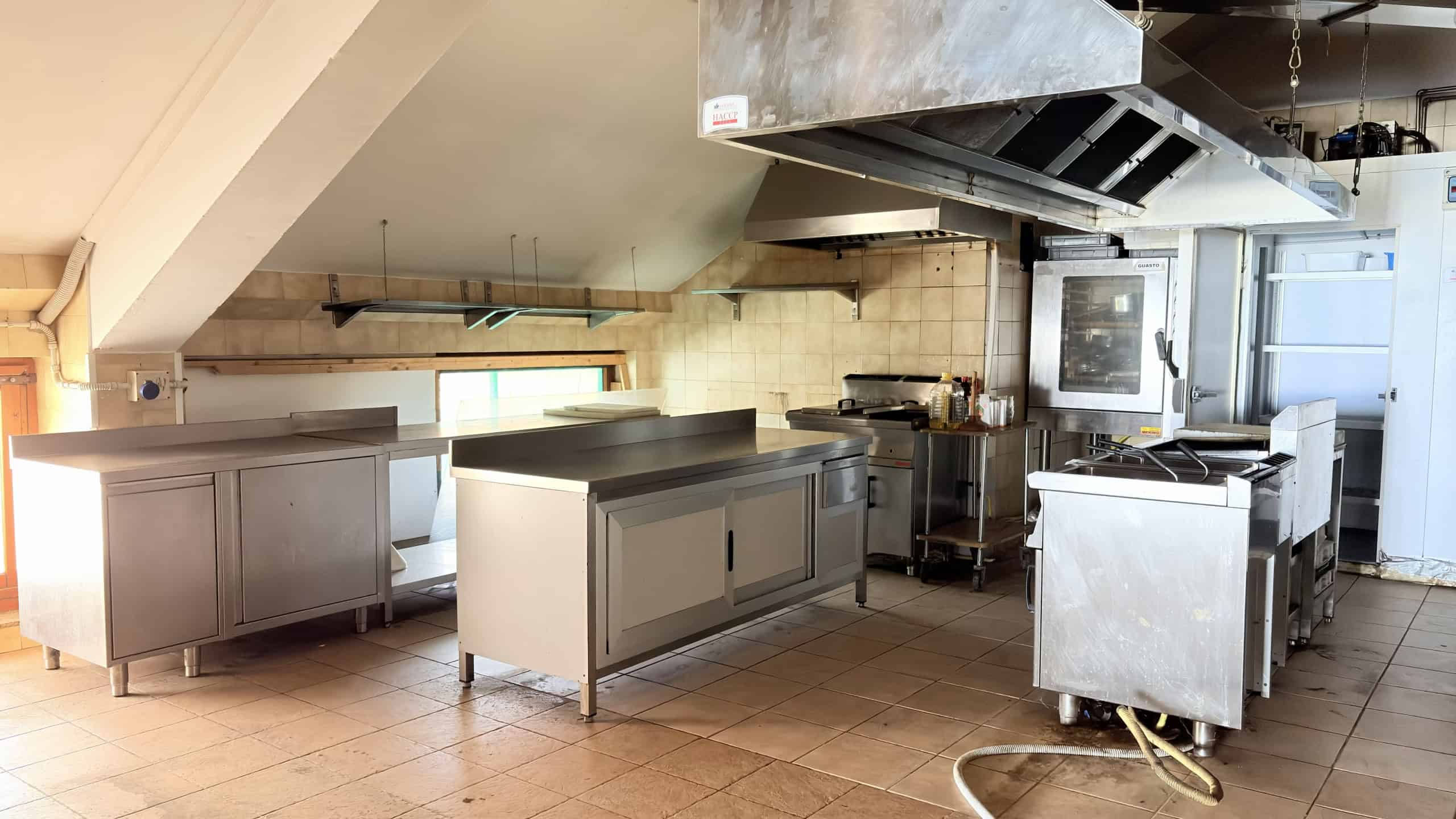 Pentole professionali in acciaio inox e apparecchi da cucina in ambiente commerciale, attrezzature cucina industriale, zona cottura e preparazione pasti, lavabo e piano di lavoro in acciaio.