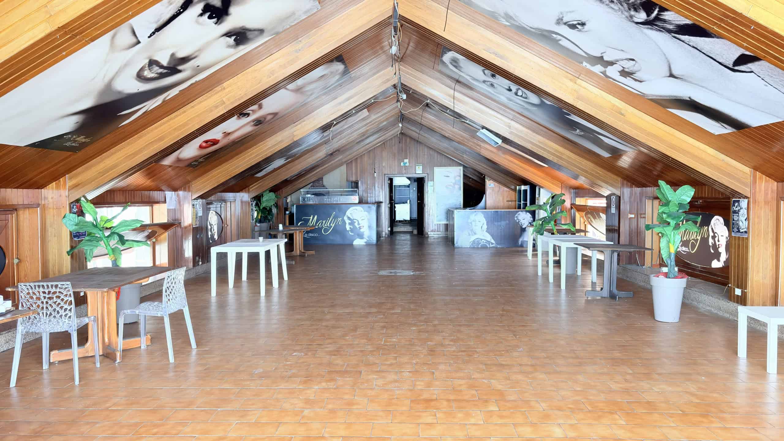 1. Interno di un locale con soffitto a doppia pendenza in legno, decorato con grandi ritratti in bianco e nero di Marilyn Monroe, ambiente moderno e accogliente.