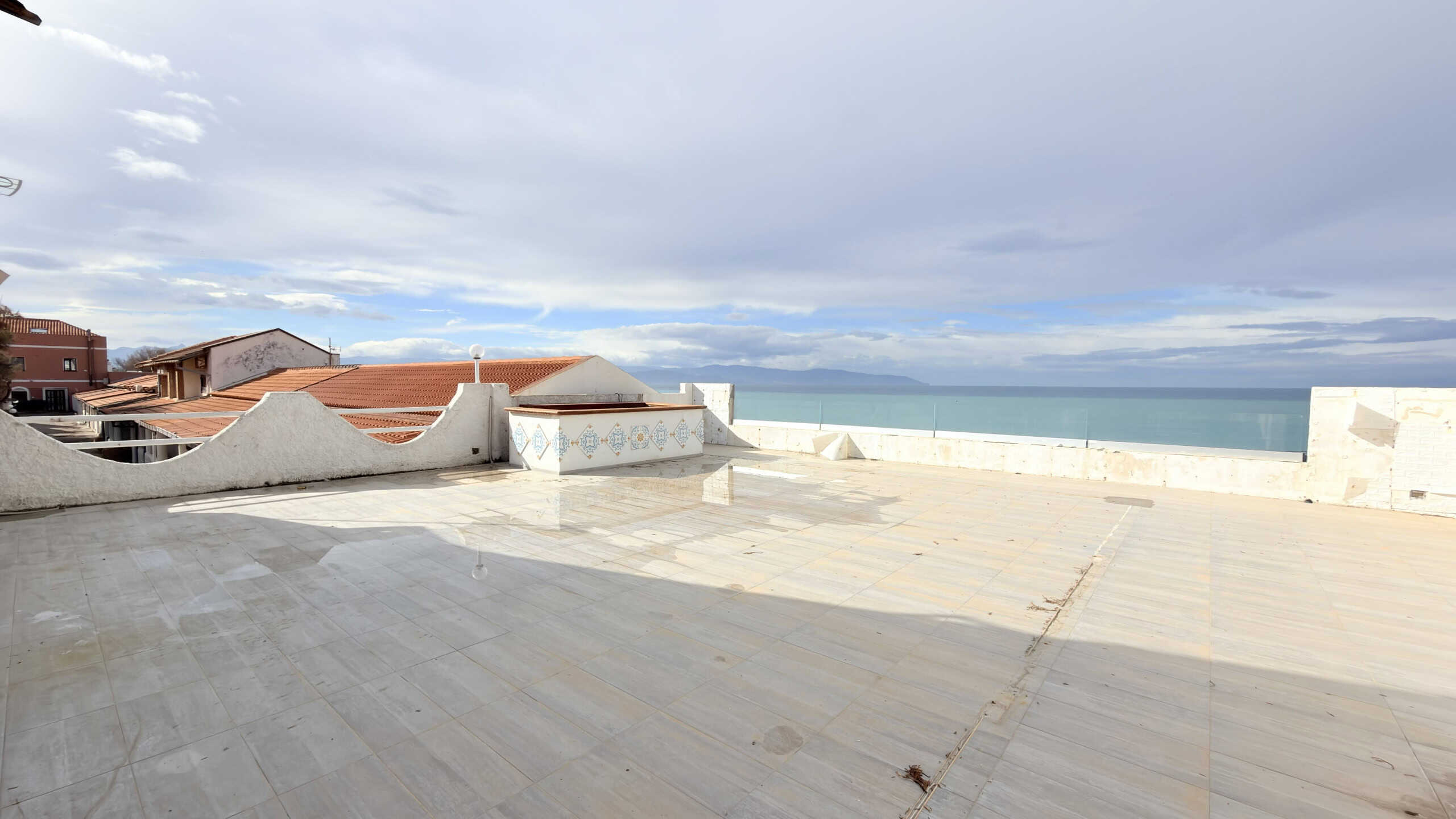 Vista panoramica su terrazza con vista mare, case in stile mediterraneo e cielo nuvoloso, ideale per immobili residenziali e attività di relax all'aperto in località costiera.
