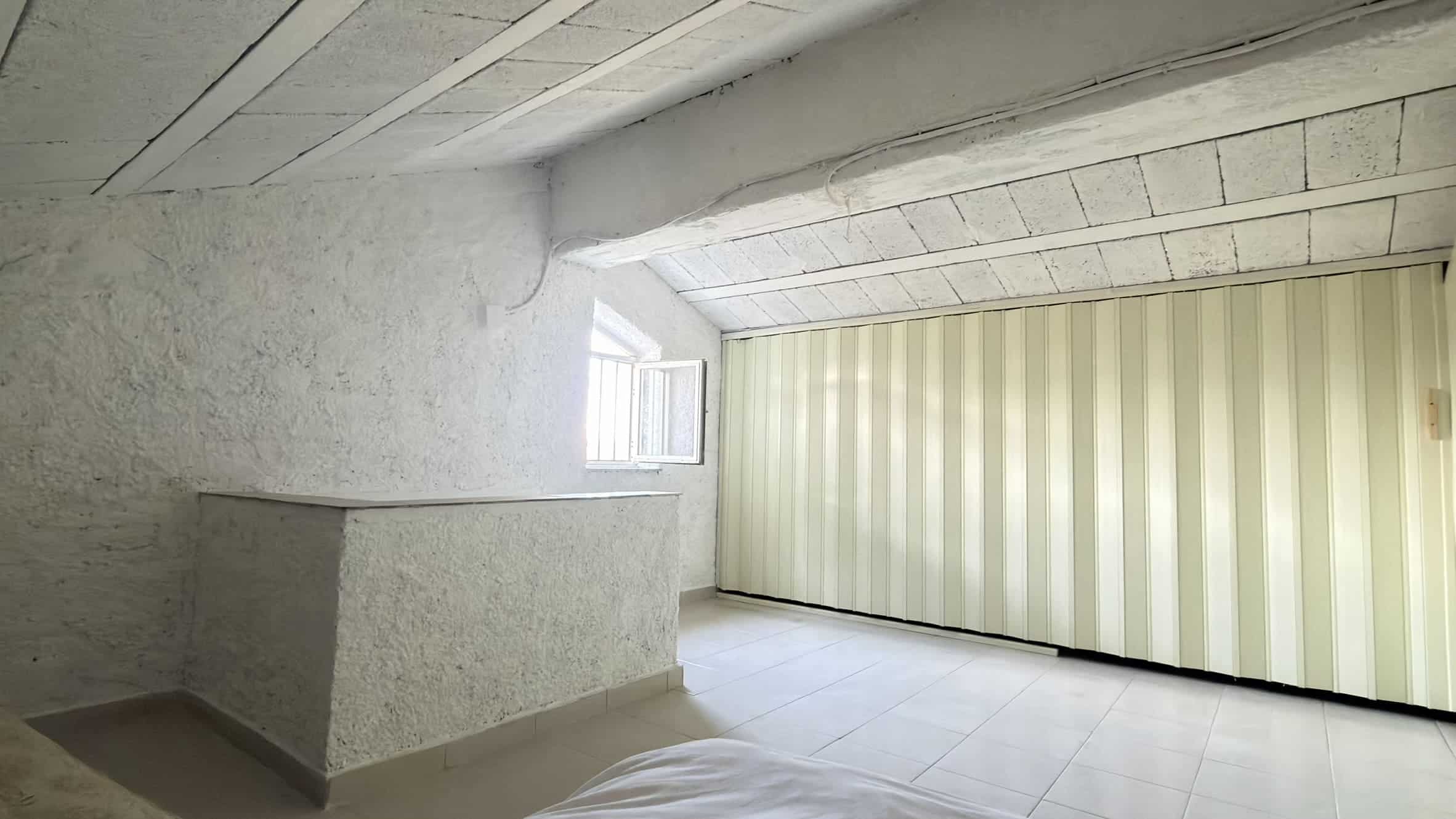 Ampia stanza mansardata ristrutturata con pareti in pietra e soffitto in legno, luce naturale, ideale per residenze o uffici, soluzione design e funzionale.