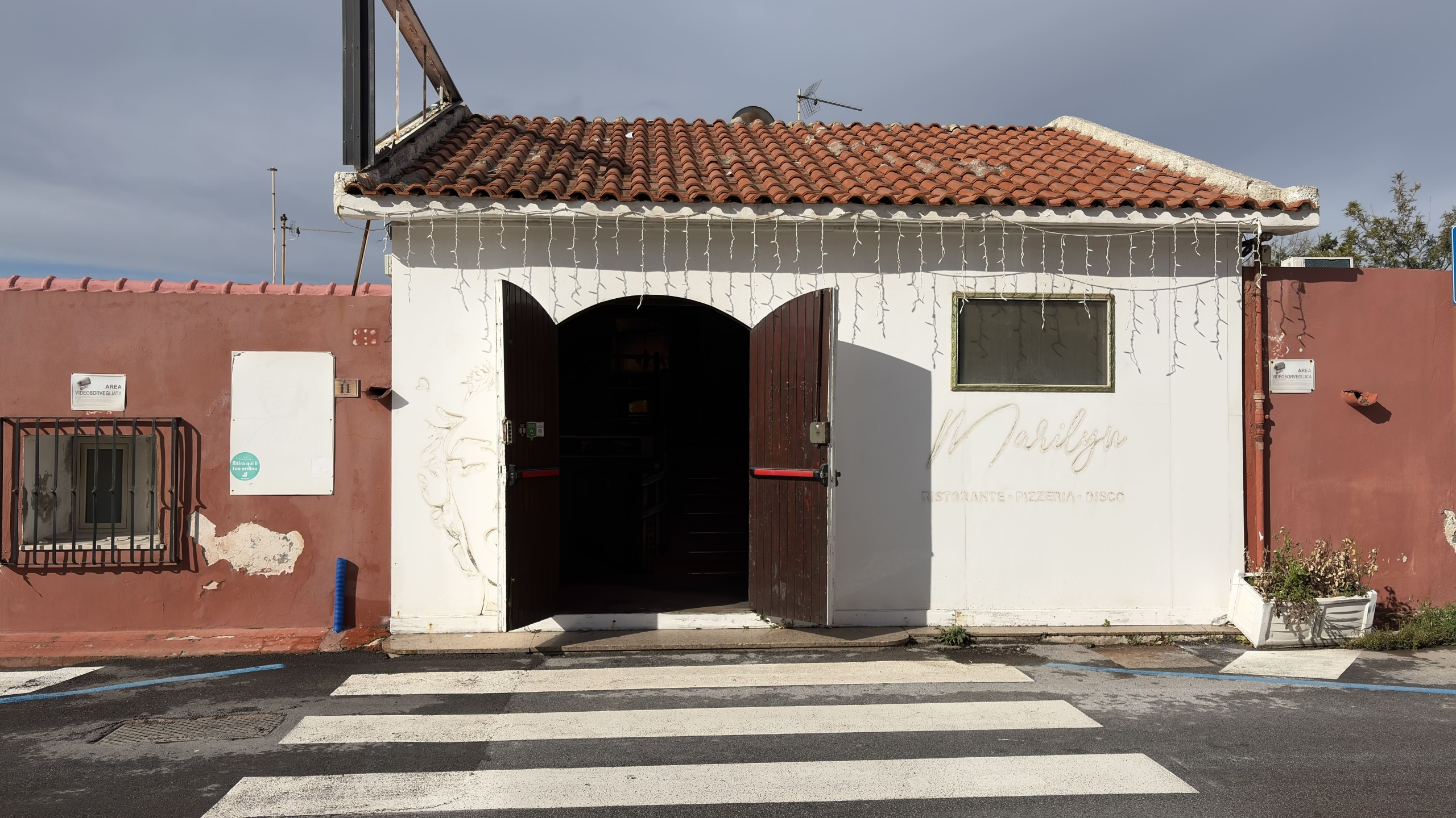 1. Casa ristorante pizzeria disco a NextCasa con facciata bianca e ingresso a ferro di cavallo, dettagli decorativi e illuminazione natalizia.