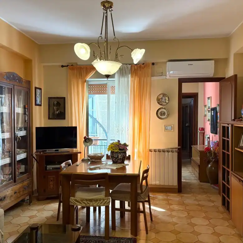 1. Appartamento arredato con soggiorno spazioso, divano, tavolo in legno, televisore e decorazioni vintage, ideale per comfort e stile abitativo.