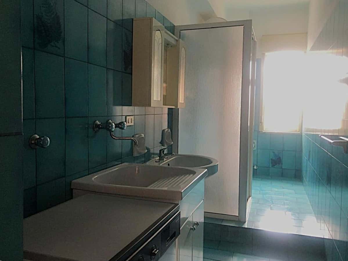 Lavabo in cucina con piastrelle verdi, spazio per lavatrice e asciugatrice, vetro opaco sulla porta, finestra che rende l'ambiente luminoso - ideale per l'acquisto di immobili con servizi essenziali.
