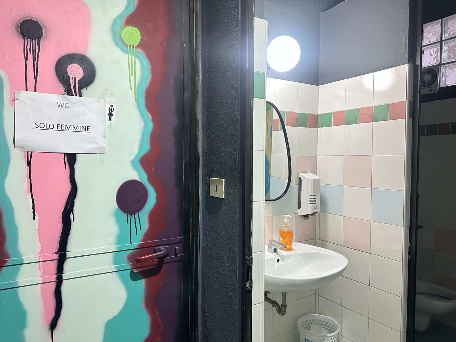 Servizi igienici femminili con pareti in piastrelle colorate e lavabo, accessibile ed elegante, in un bagno di un locale pubblico con pareti decorate artisticamente.