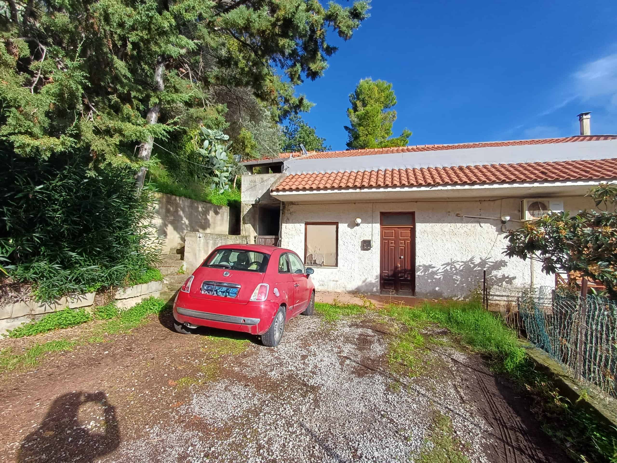 Auto rosso parcheggiato davanti a casa unifamiliare in stile rustico, con giardino e ambiente naturale, in felice zona residenziale.