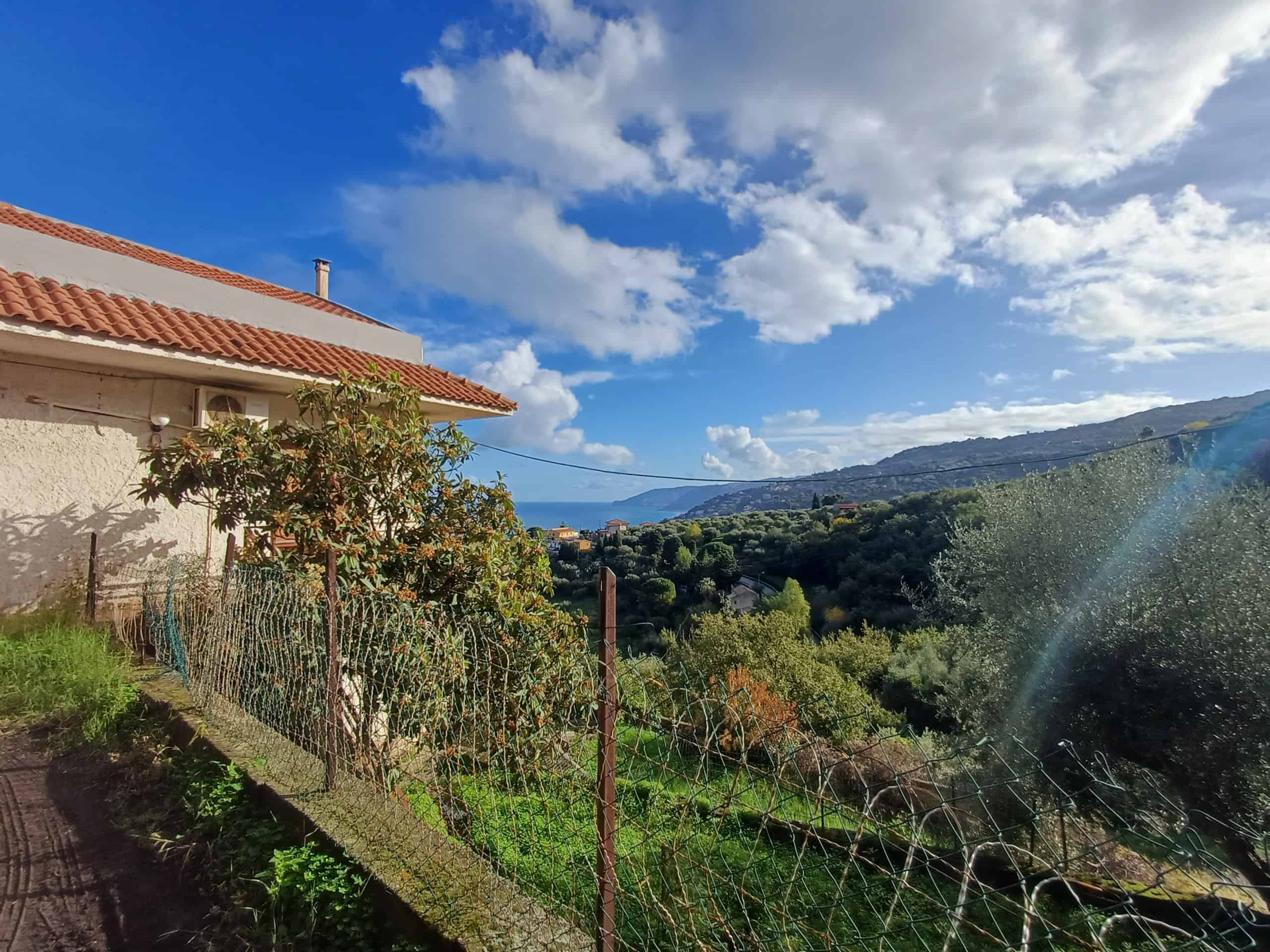 Paesaggio suggestivo con vista mare e colline, casa con terrazza soleggiata, cielo sereno e natura rigogliosa in Toscana, ideale per investimenti immobiliari e case vacanza.