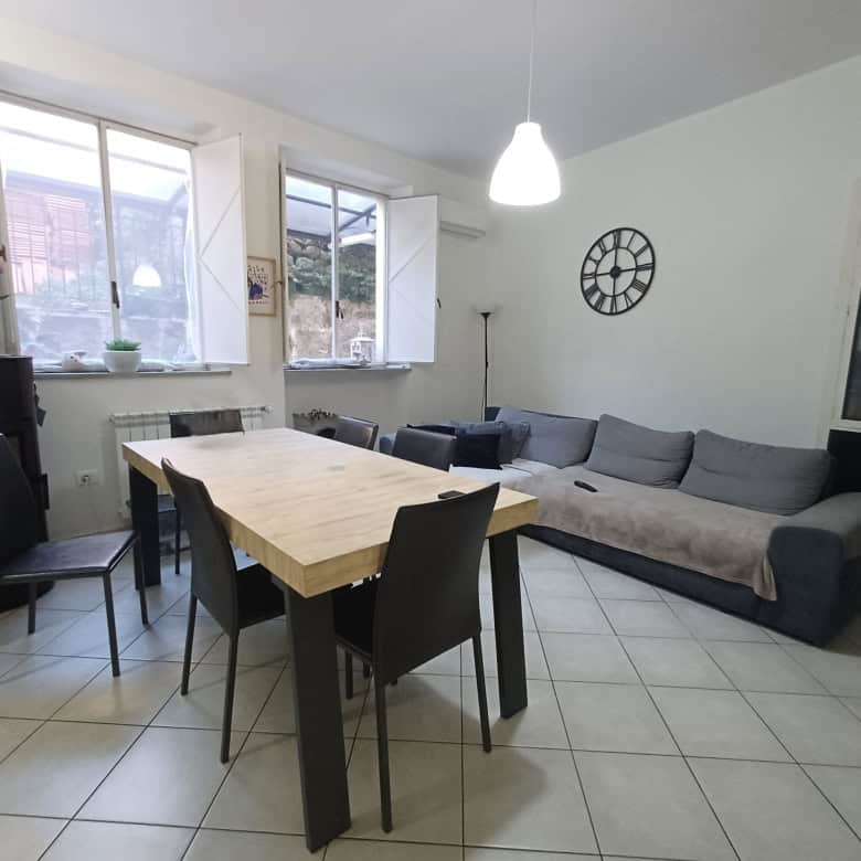 Accogliente soggiorno con tavolo in legno, divano grigio, grandi finestre e decorazioni moderne, ideale per vivere e condividere momenti di relax in casa.