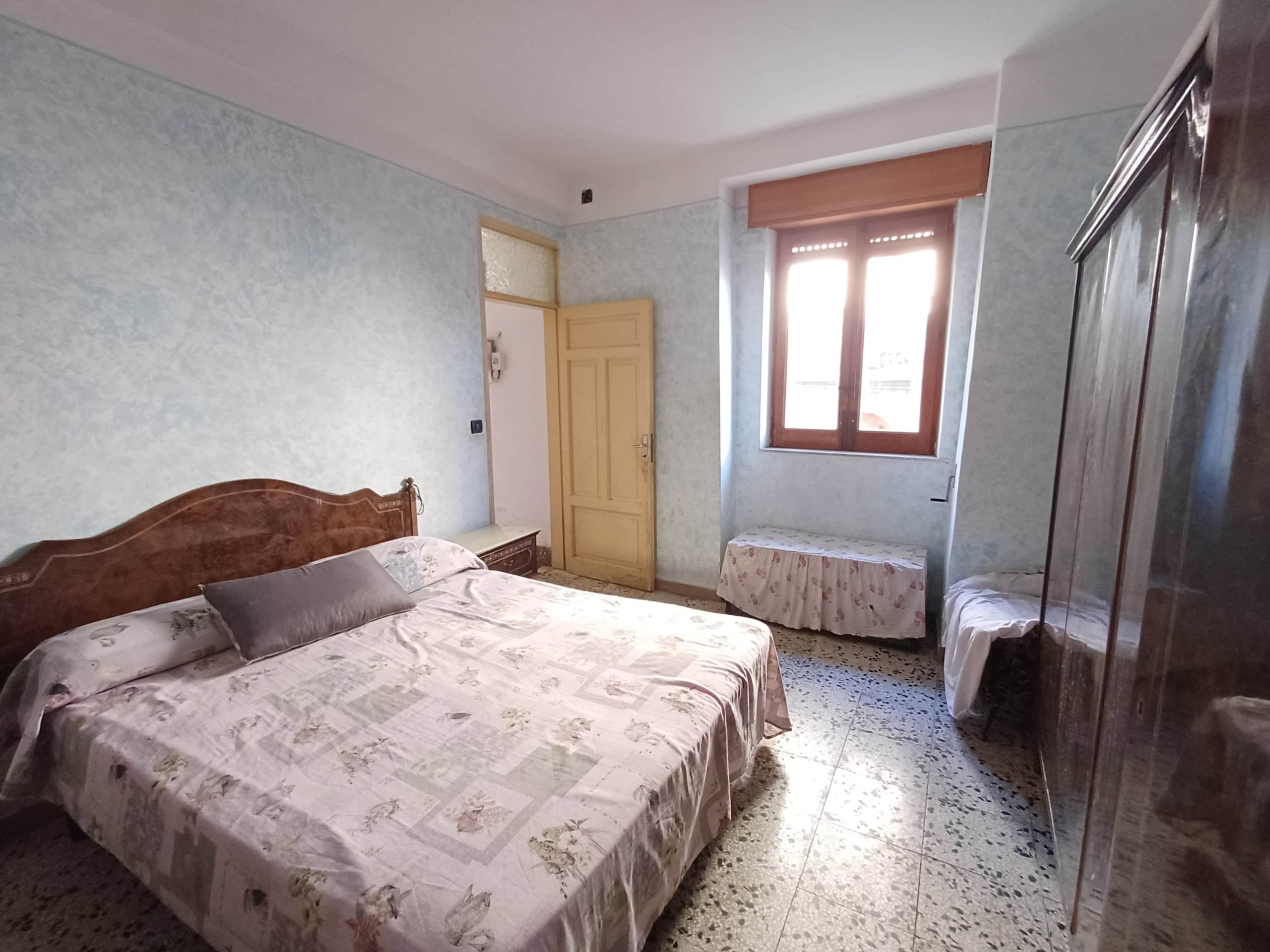 1. camera da letto con letto matrimoniale, armadio in legno e finestra con inferriata, stile classico, arredamento antico, luce naturale.