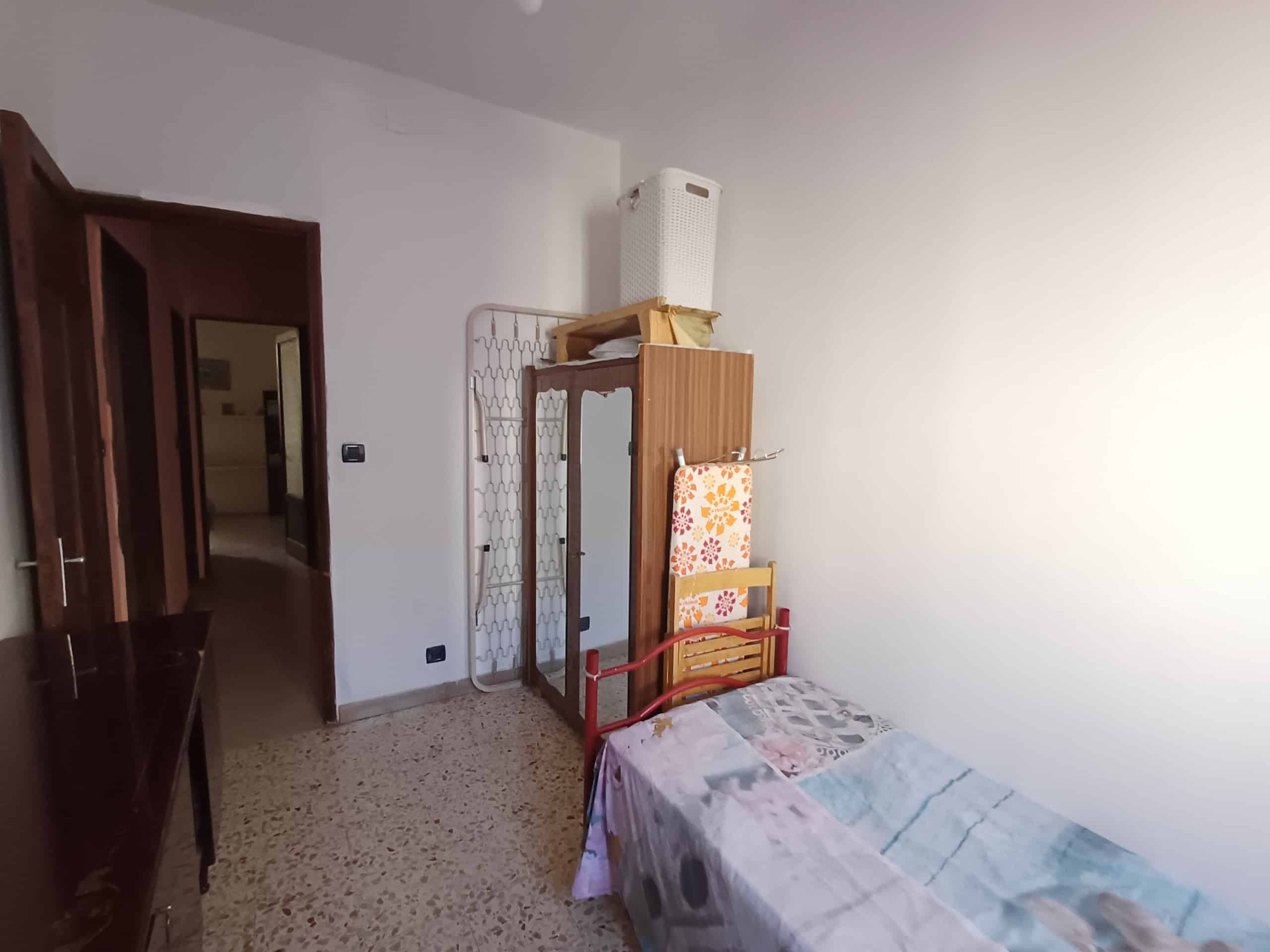 Arredamento semplice e funzionale in una camera da letto con letto singolo, armadio e accessori essenziali, ideale per soluzioni di affitto residenziale a NextCasa in Italia.