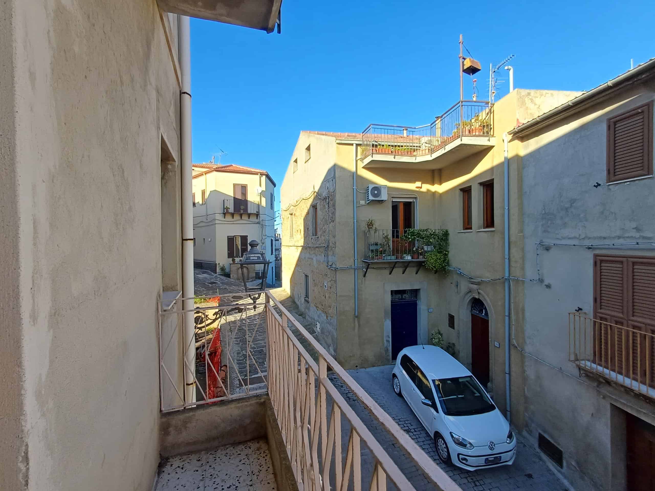 Vista di un vicolo antico e caratteristiche case in pietra, centro storico di un paese italiano, con strada pavimentata e auto parcheggiate, scenario autentico e suggestivo da NextCasa.