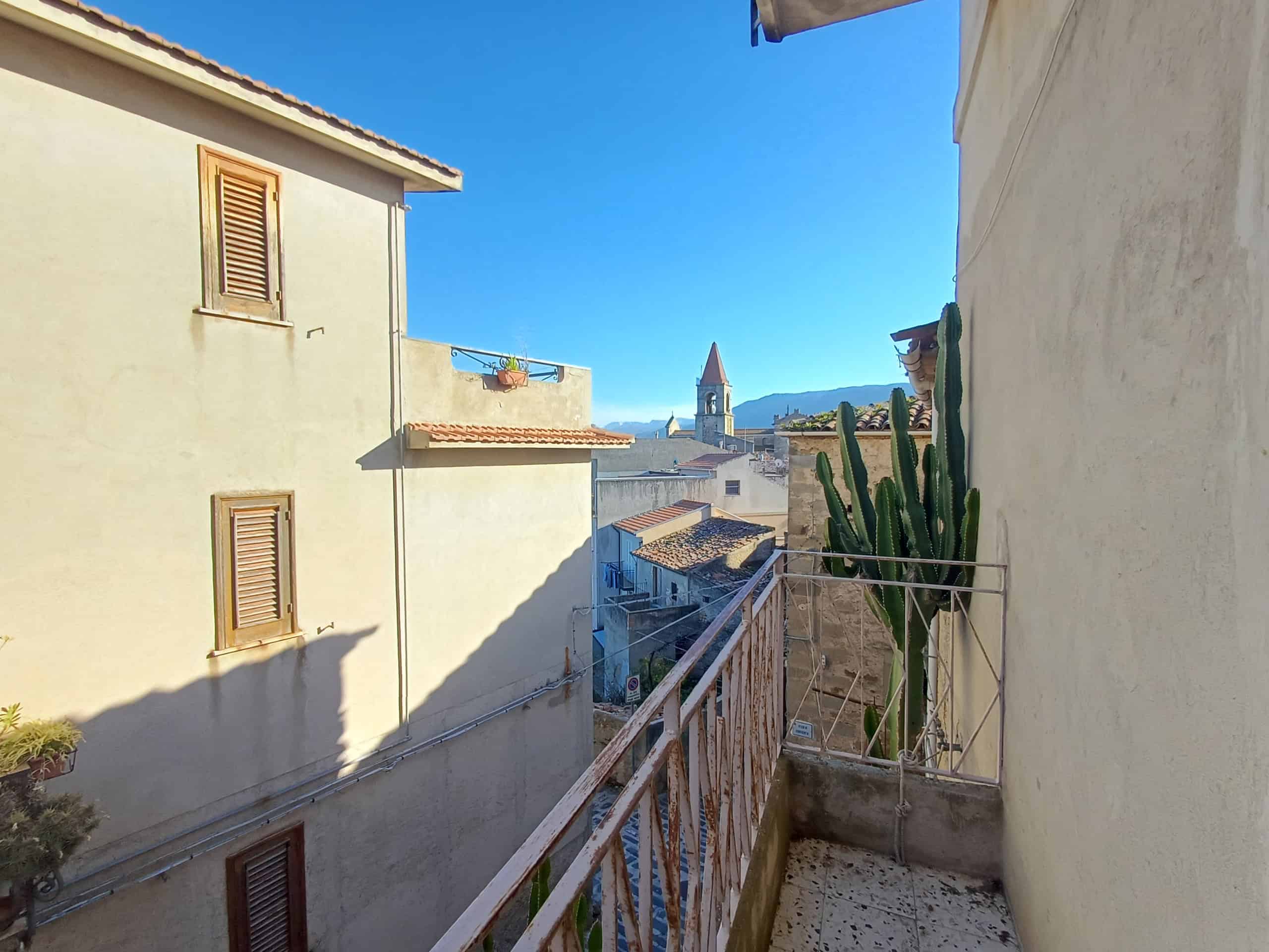 Vista balcone con cactus, tetti e chiesa in lontananza in un tipico quartiere italiano, ideale per case in vendita o in affitto a NextCasa.