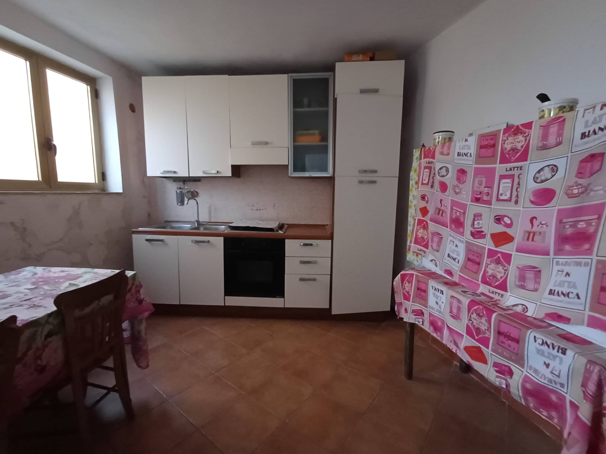 1. Cucina compatta con mobili bianchi, lavabo e forno in un ambiente rustico e semplice.