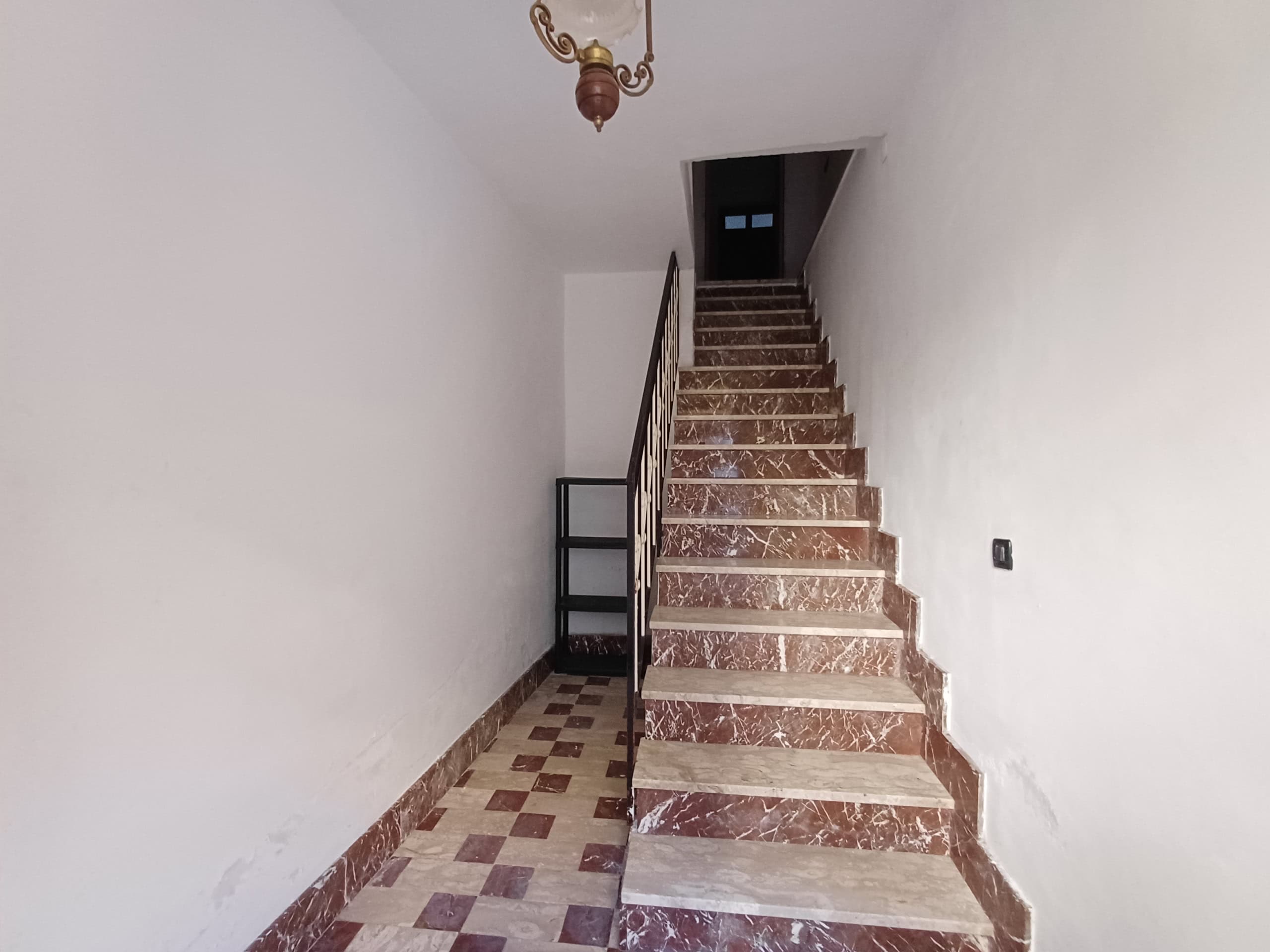 Scala in marmo con ringhiera in metallo, ingresso di un appartamento, interni moderni con pareti bianche, pavimento in gres, illuminazione a soffitto, spazio elegante e funzionale.