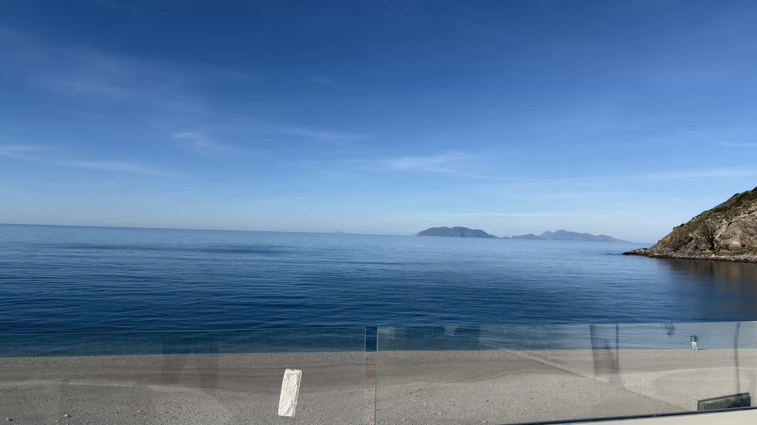 Spiaggia con vista mare cristallino e isole sullo sfondo, paesaggio marino italiano, mare blu calmo, costa rocciosa, zona balneare, relax e vacanze al mare.