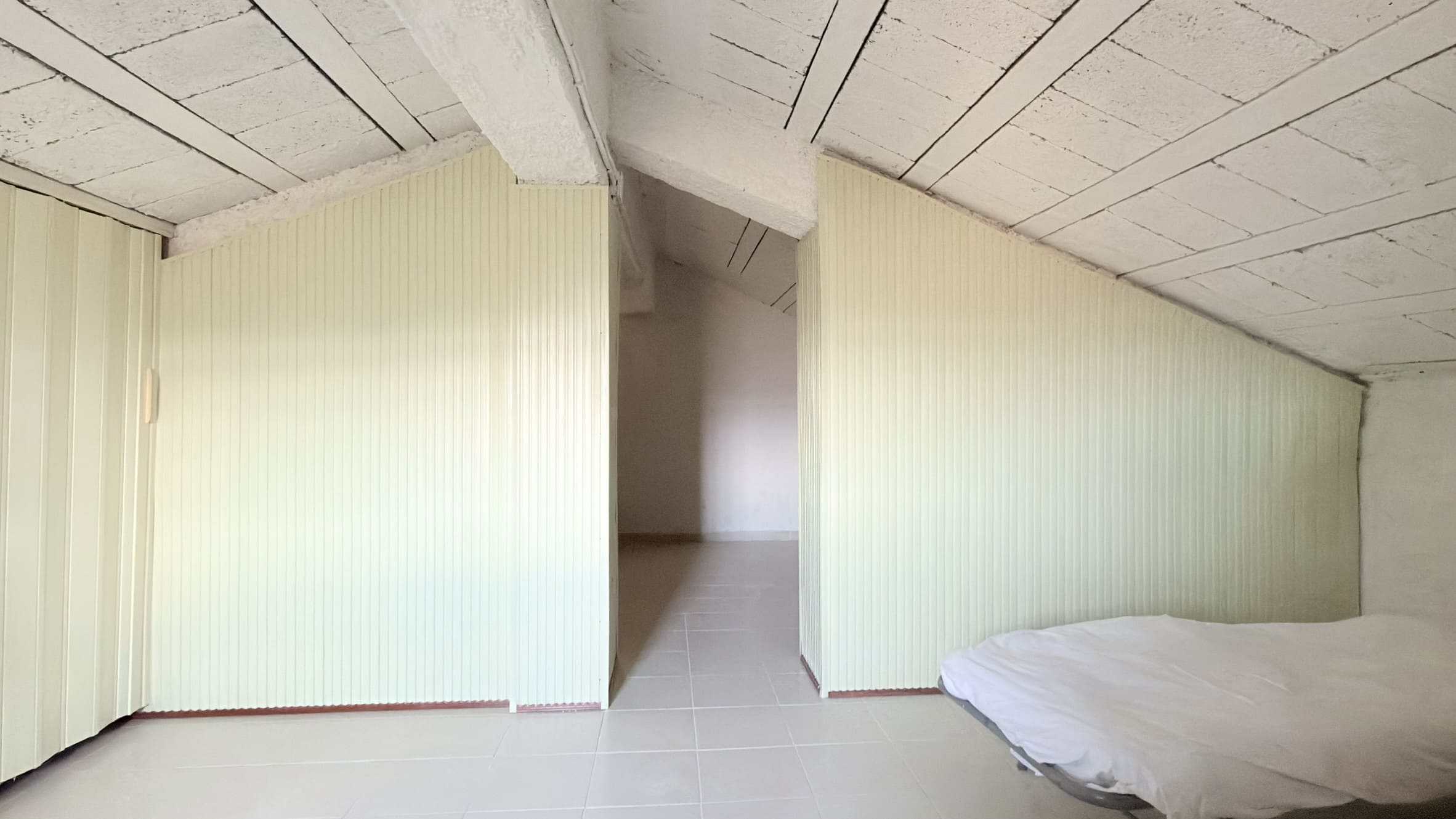 Soffitta abitabile con pareti rivestite in legno e tetto in cemento armato, ambiente rustico e accogliente ideale per ristrutturazione e utilizzo come spazio living o camera da letto.