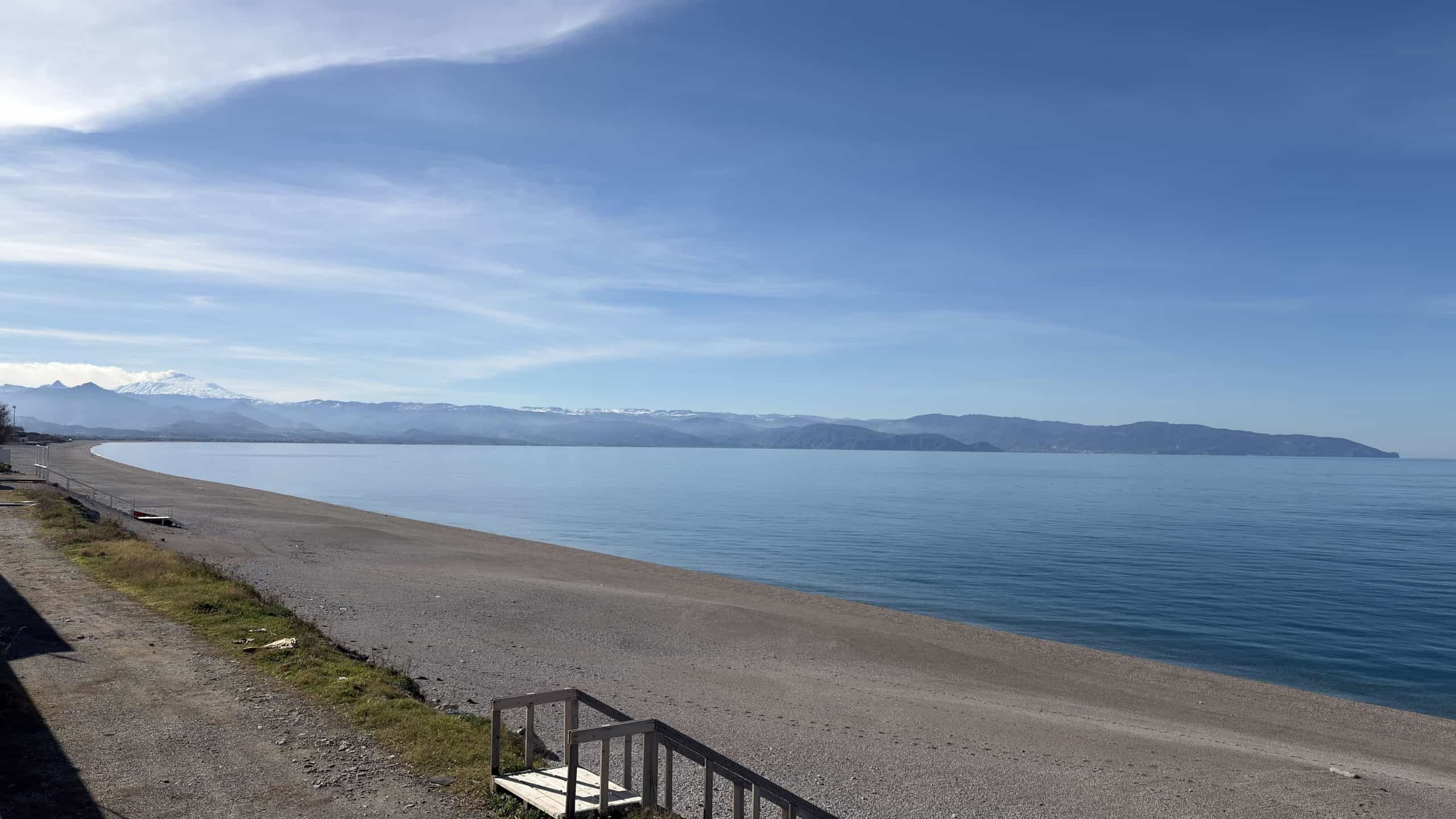 Spiaggia sul lago con vista sul mare, montagne e cielo sereno, luogo ideale per immobili residenziali e investimenti immobiliari, scenario naturale di grande fascino.