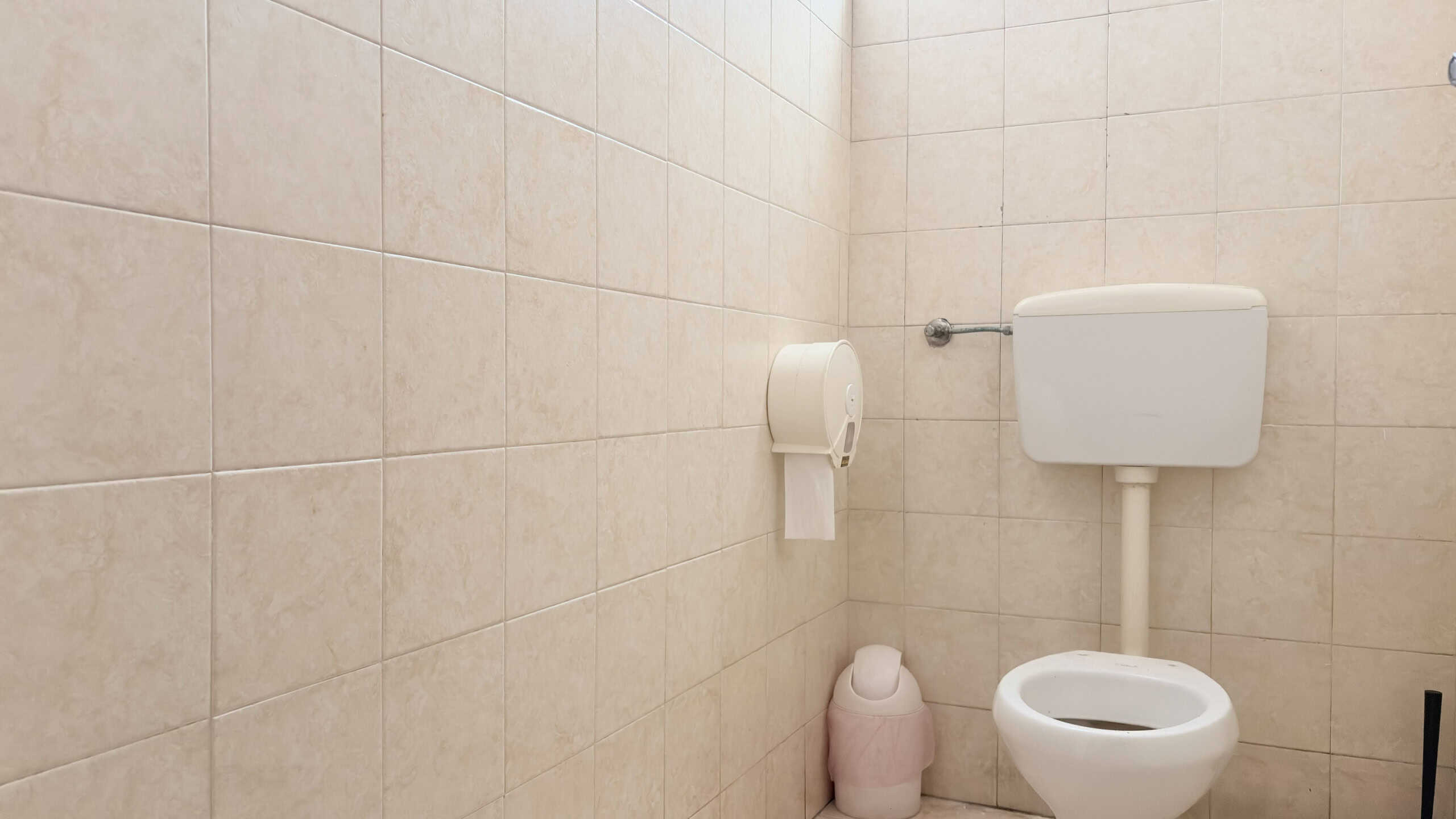 Specchio a parete con servizi igienici e carta igienica in bagno pubblico con piastrelle beige moderne.